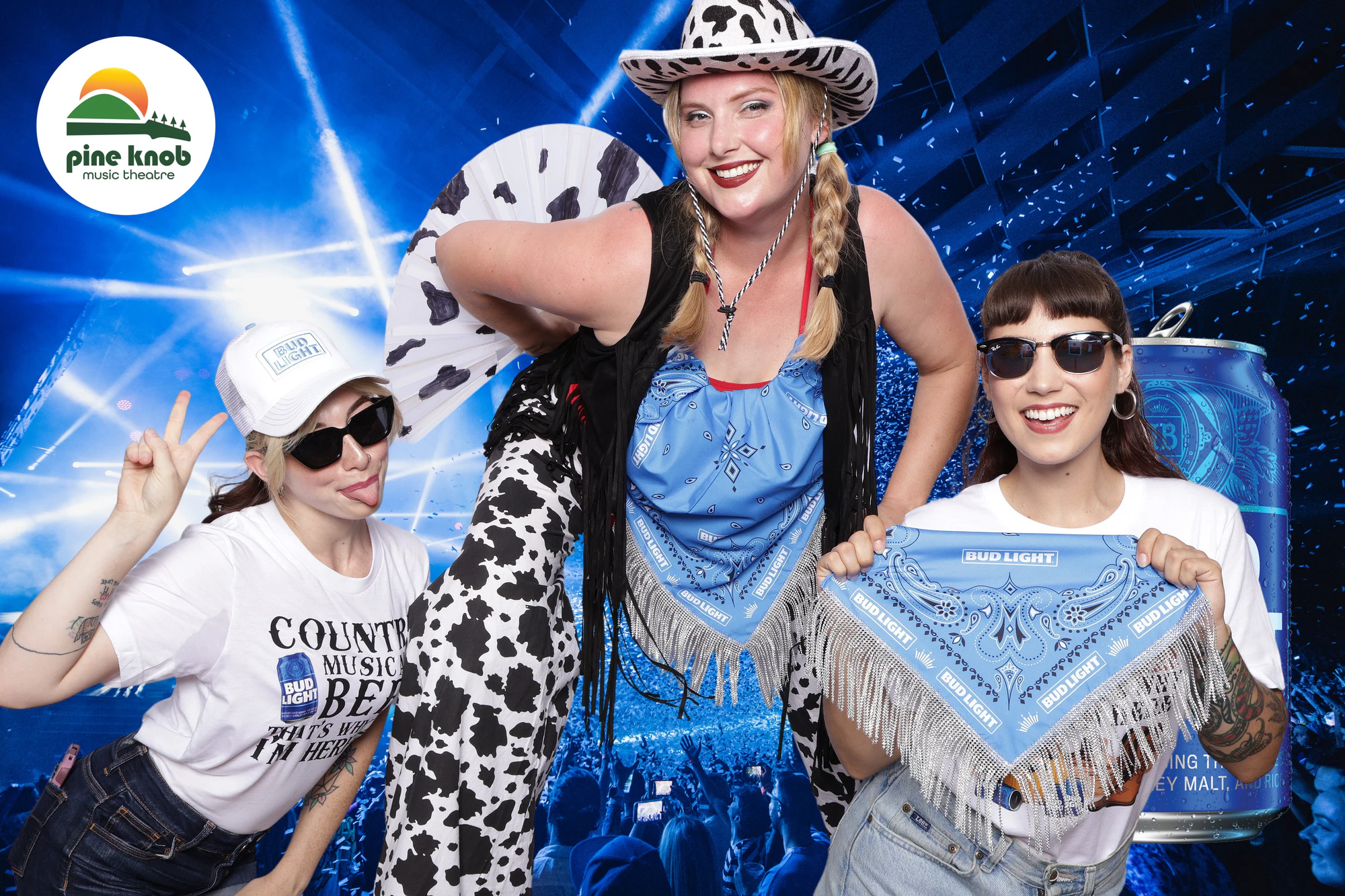 Three guests, one in a cow-print hat and chaps, the others stretching out a Bud Light bandana at Bud Light Tailgate at Pine Knob, 2024