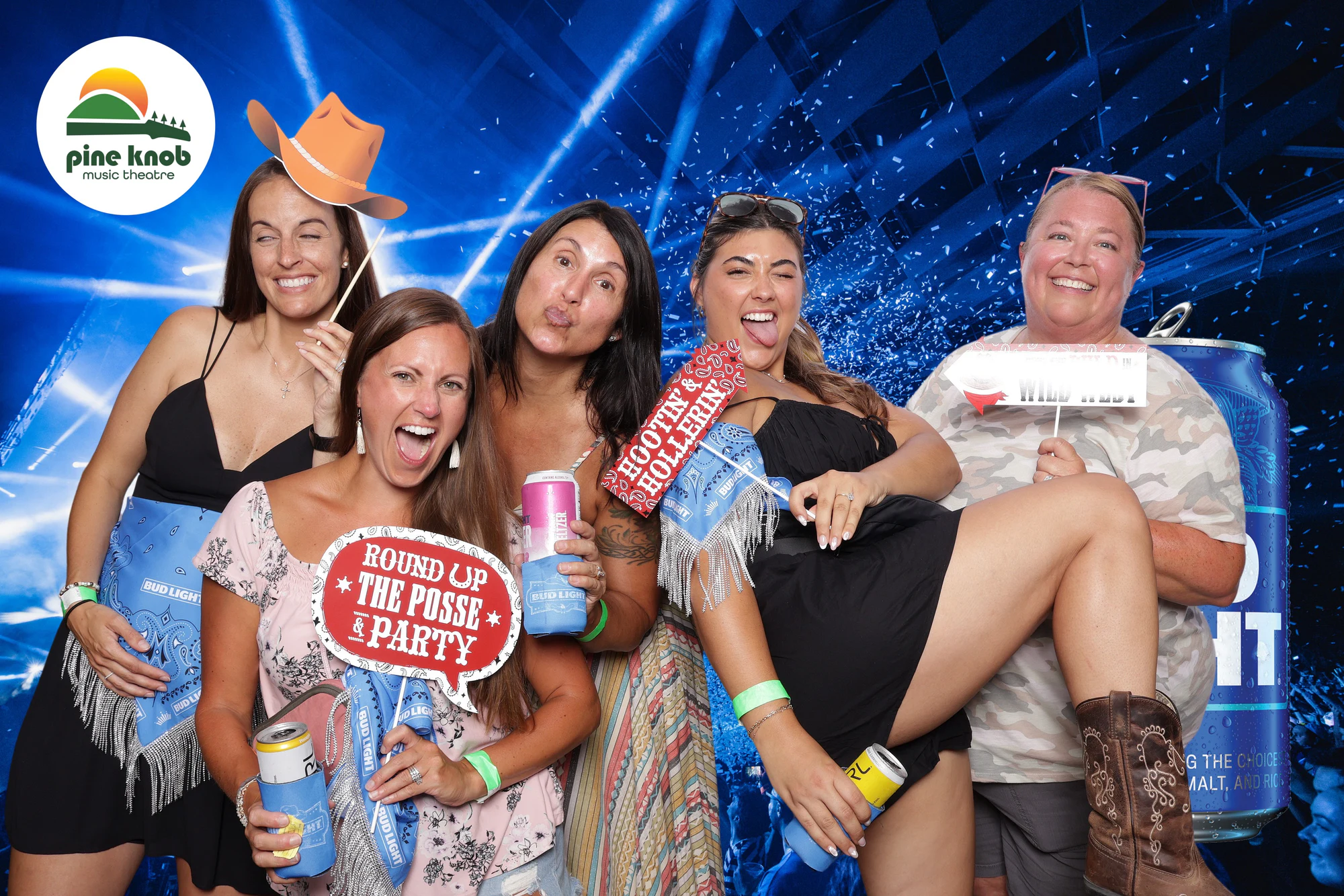 Five guests with cans and signs, one hoisted off her feet in cowboy boots at Bud Light Tailgate at Pine Knob, 2024