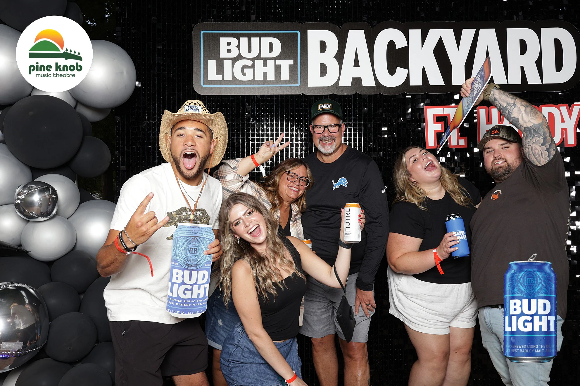 Six guests at the Backyard sign, one in a straw cowboy hat holding an oversized can at Bud Light Tailgate with 313 Presents, 2025