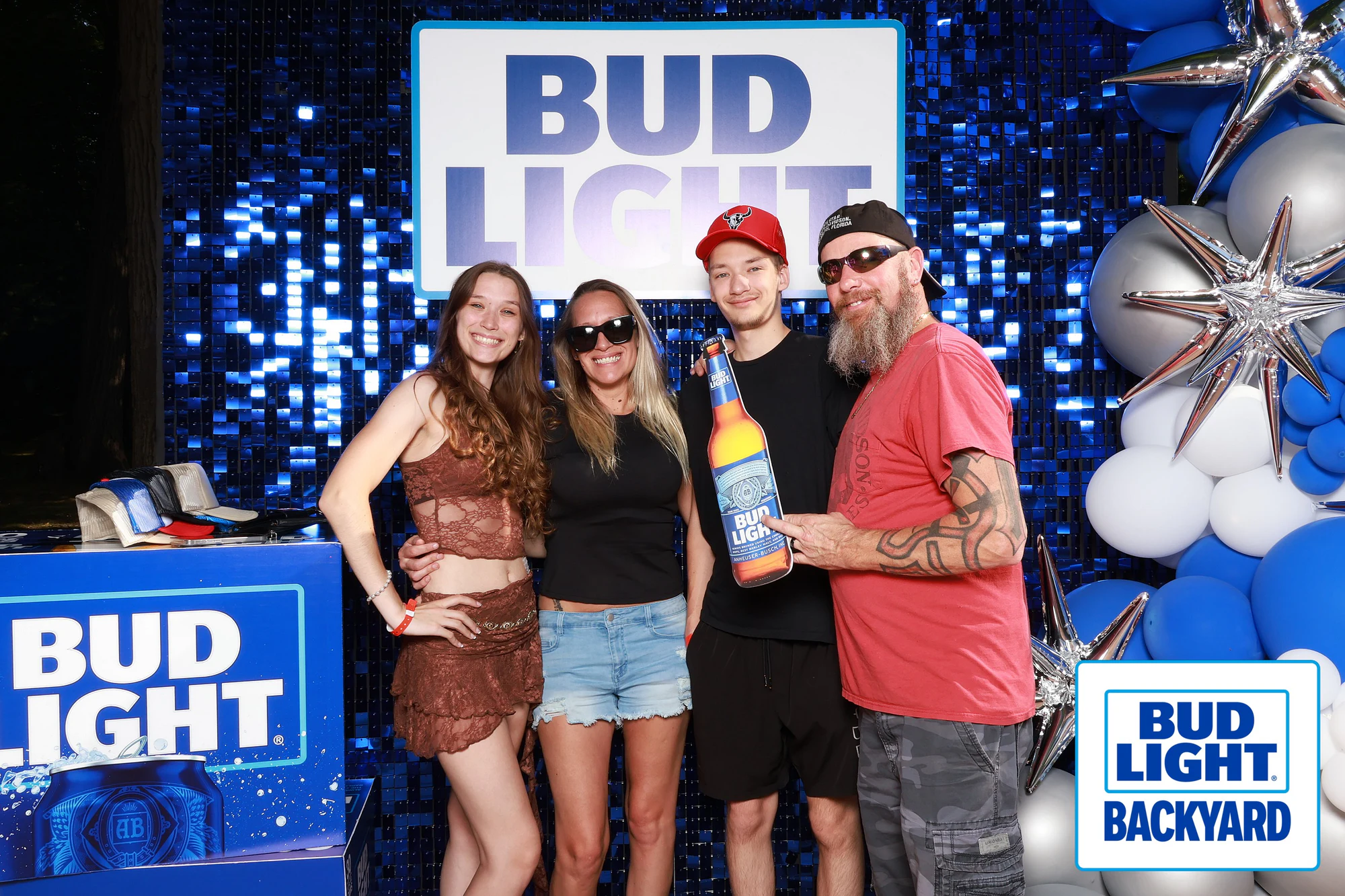 Four guests at the sequin wall, one holding an oversized Bud Light bottle at Bud Light Tailgate for Luke Bryan, 2026