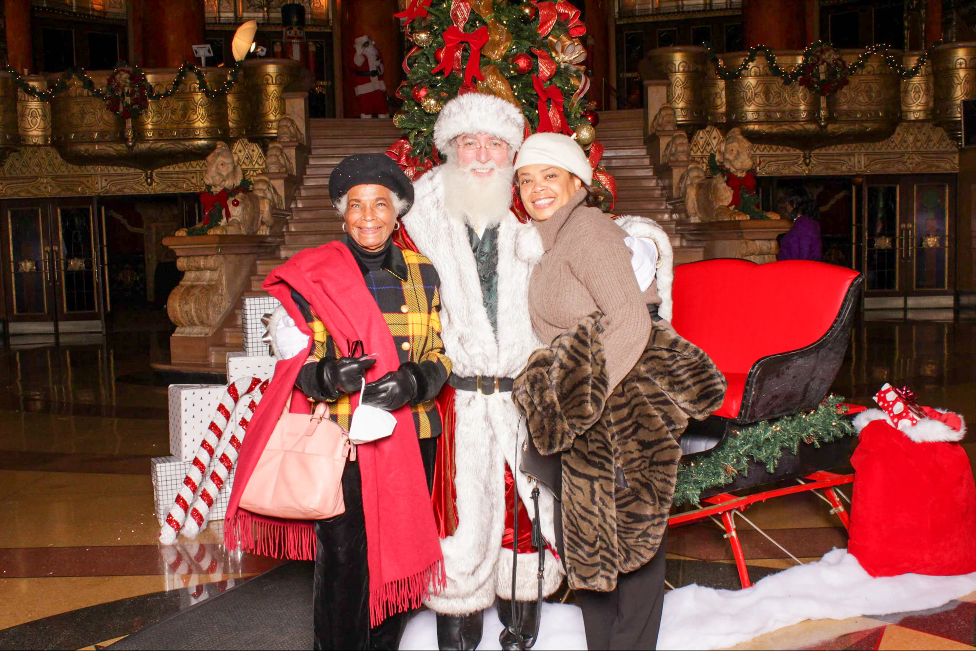 Two guests in winter coats with Santa in front of the lobby tree at 313 Presents Holiday Event at the Fox Theatre