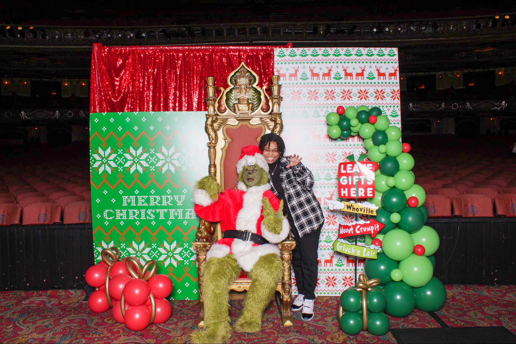 A guest in a plaid jacket with an arm around the Grinch on the throne at 313 Presents Holiday Event at the Fox Theatre