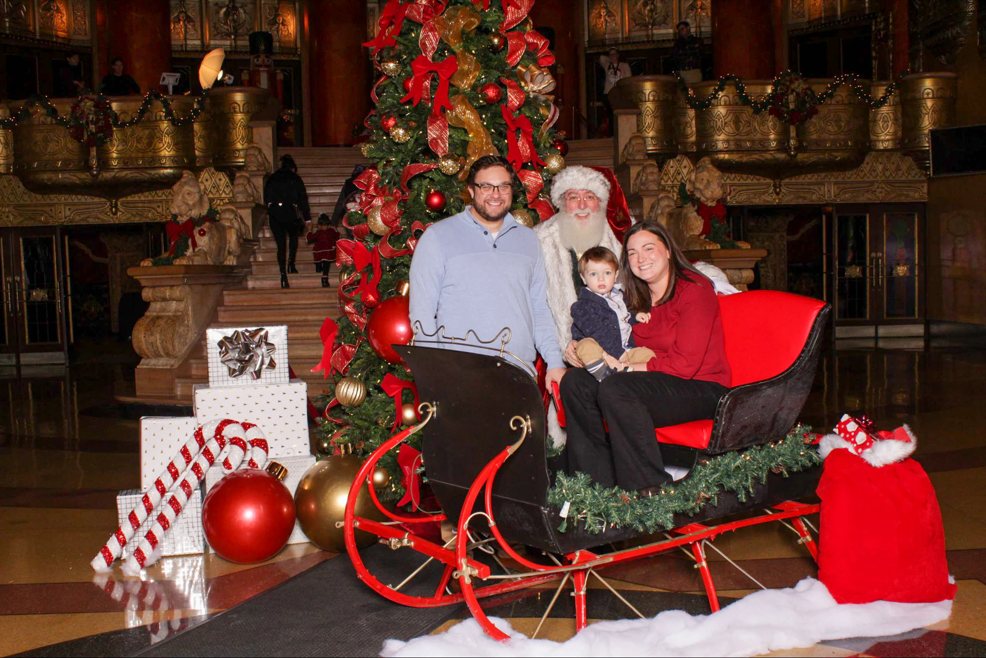 A couple in the red sleigh with a toddler between them and Santa behind at 313 Presents Holiday Event at the Fox Theatre