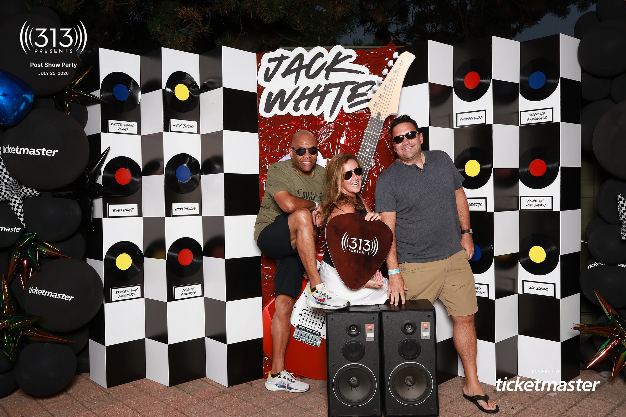 Three guests around the big 313 guitar pick, one crouched in front at Jack White Post-Show Party at Pine Knob