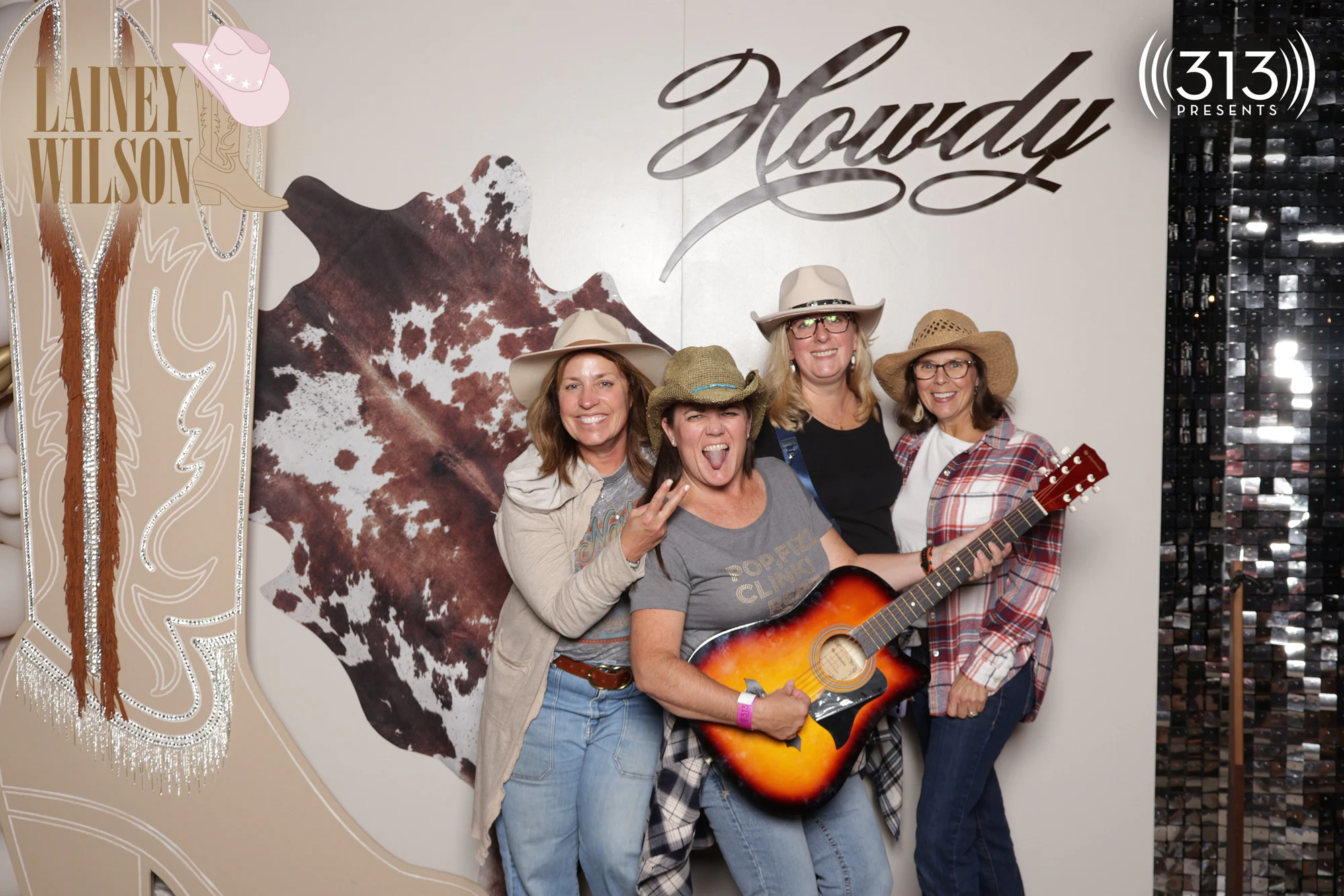 Four guests in cowboy hats, one crouched with the guitar and her tongue out at Lainey Wilson with 313 Presents