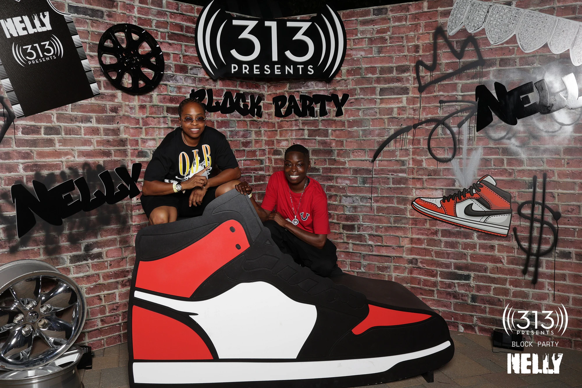 Two guests leaning on the giant sneaker, both mid-laugh at Nelly Block Party with 313 Presents