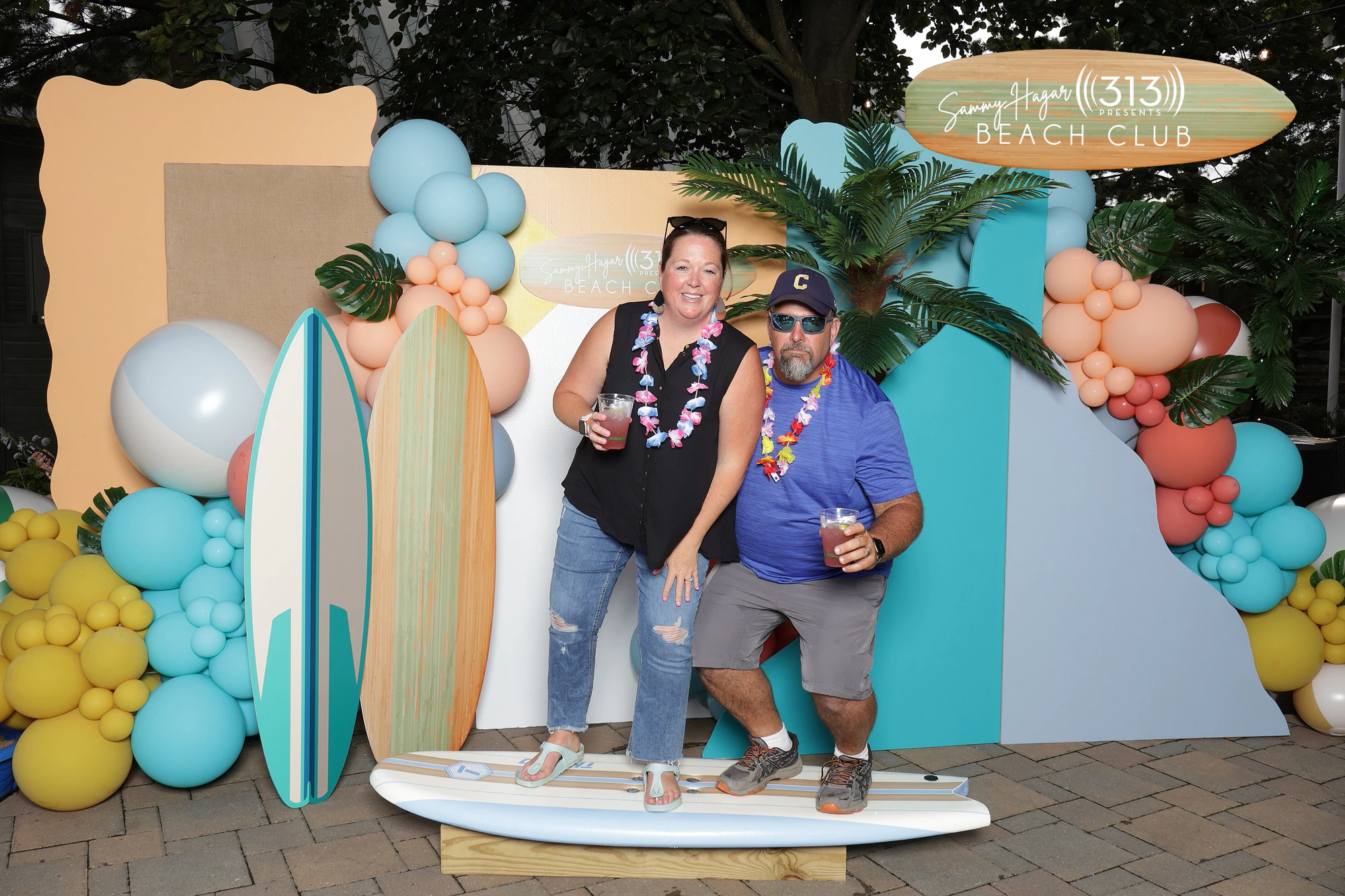 Two guests in flower leis standing on the surfboard with drinks at Sammy Hagar at Pine Knob with 313 Presents