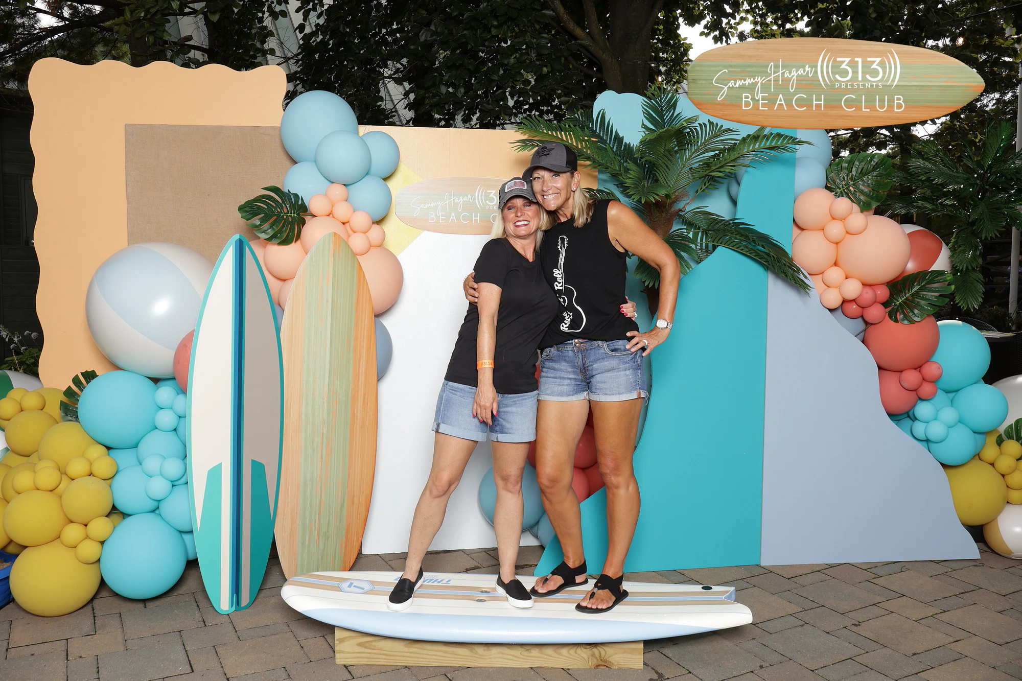 Two guests leaning together on the surfboard in front of the balloon wall at Sammy Hagar at Pine Knob with 313 Presents
