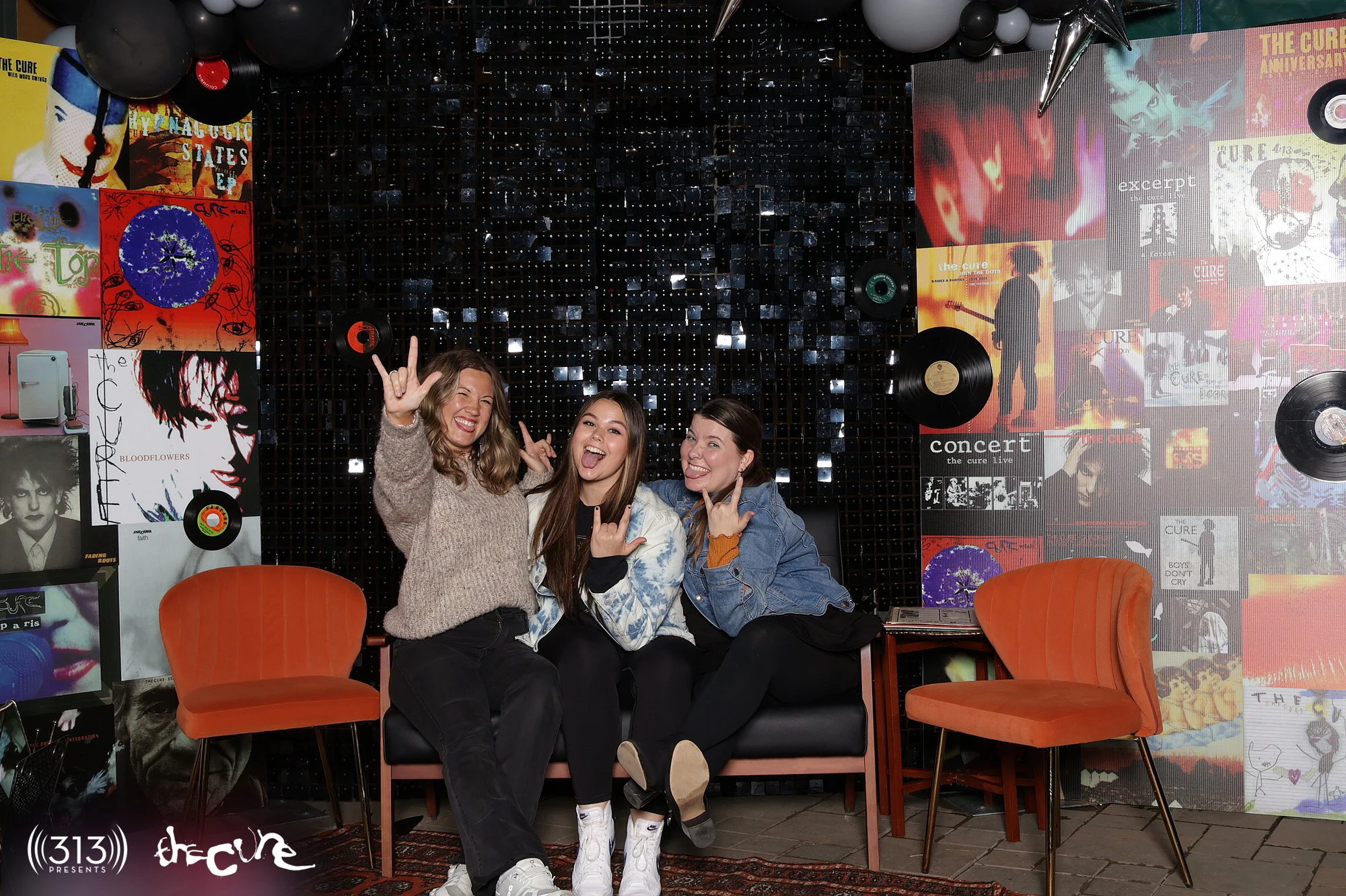 Three guests on the couch throwing peace signs, one holding a record at The Cure VIP Party with 313 Presents