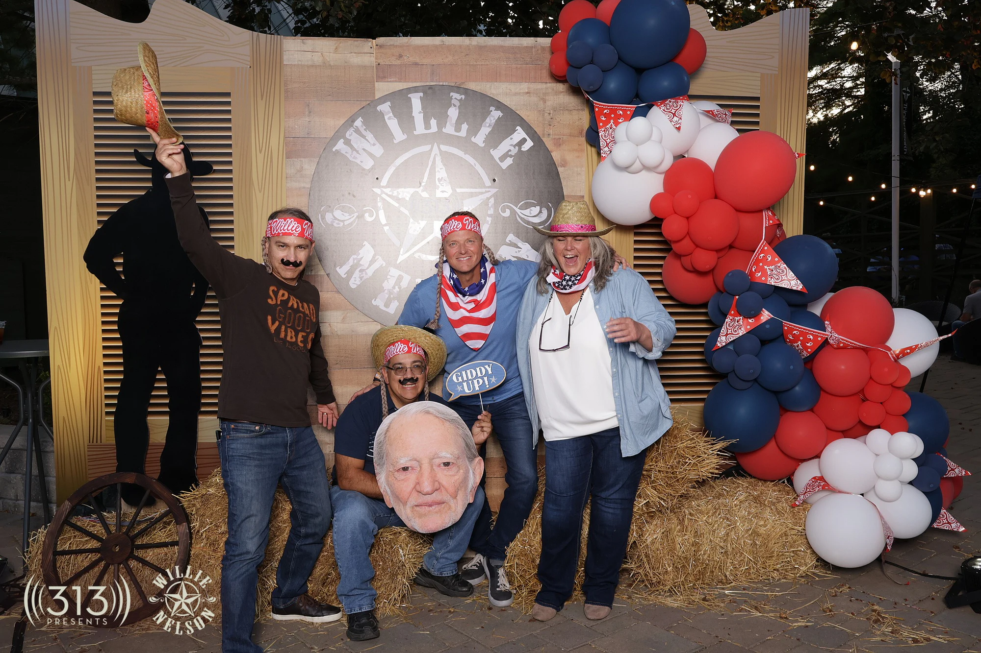 Four guests at the Willie sign, one crouched with the Willie cutout, one waving a straw hat at Willie Nelson VIP Party with 313 Presents