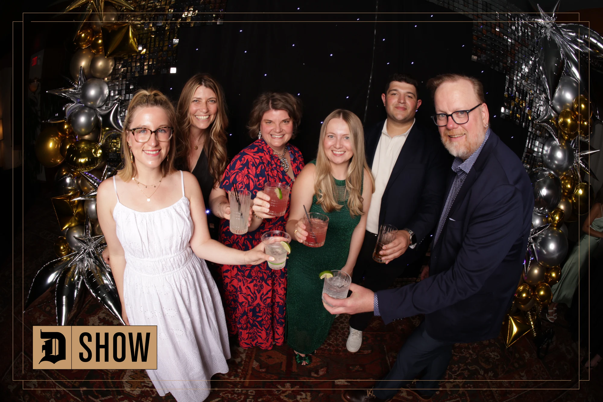 Six guests with drinks under the balloon arch at The D Show 2024