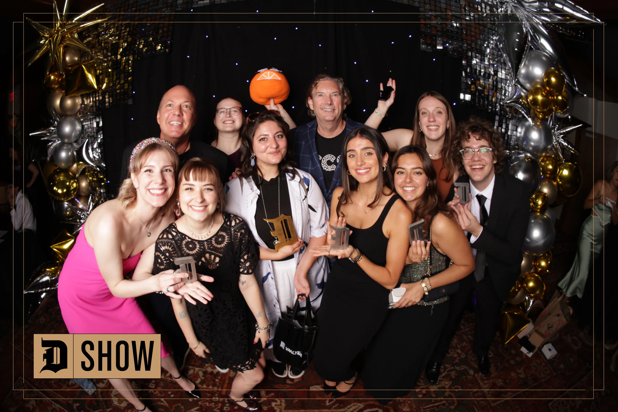 A group of ten crowded in under the balloon arch, one holding a trophy at The D Show 2024