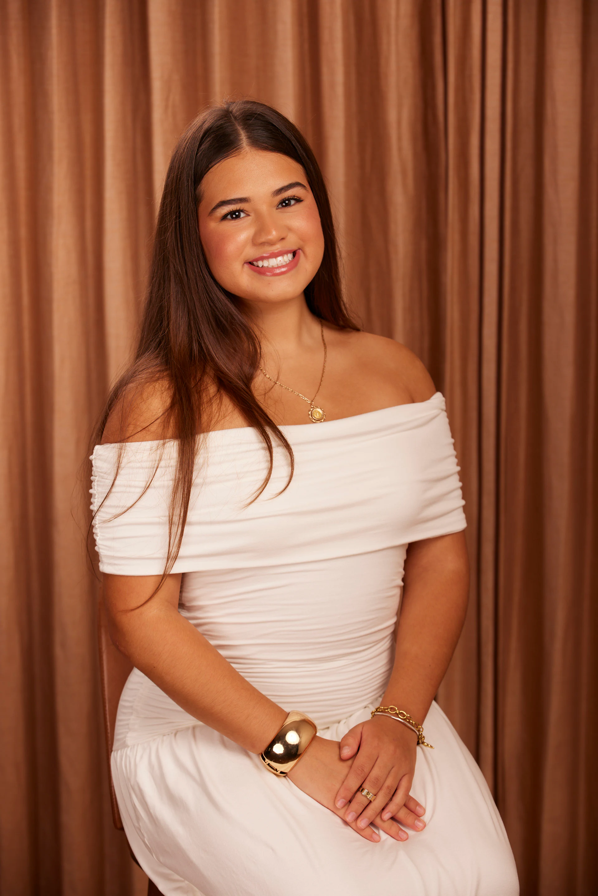 A seated portrait of a guest in a white off-the-shoulder dress, hands folded at Adcraft Detroit headshots at Shinola Hotel