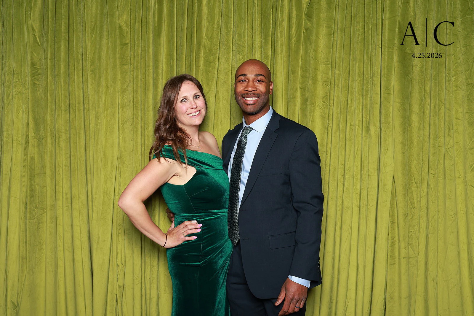 A woman in an emerald velvet dress with her hand on her hip and a man in a navy suit in front of the olive green velvet at the Andrew + Conor wedding