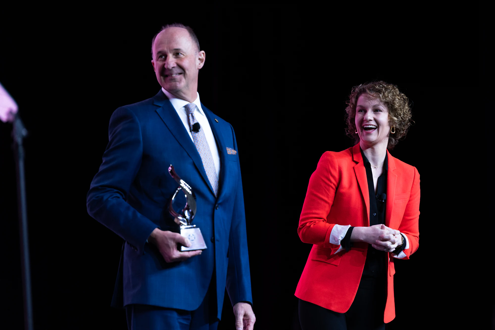 An award handed over on stage, the presenter in red at Autodesk at the AGC Annual Convention 2023