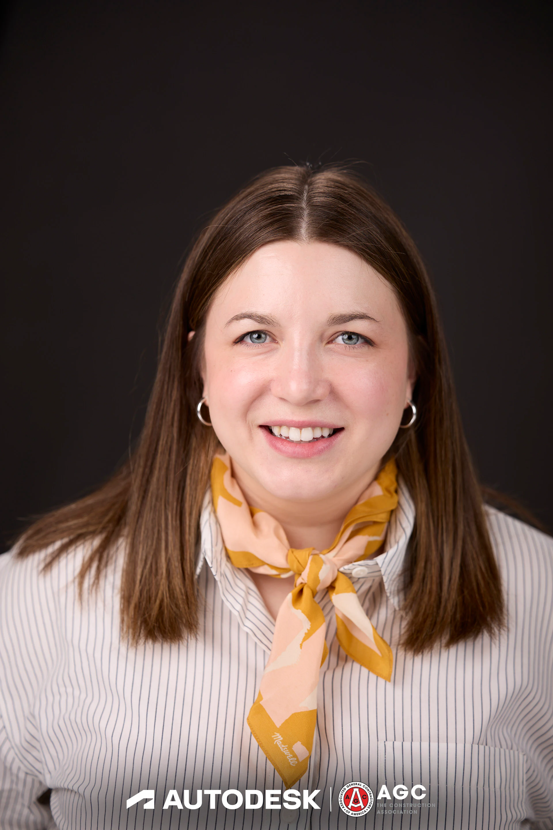 A headshot of a guest in a striped shirt and a yellow scarf at Autodesk at the AGC Annual Convention 2025