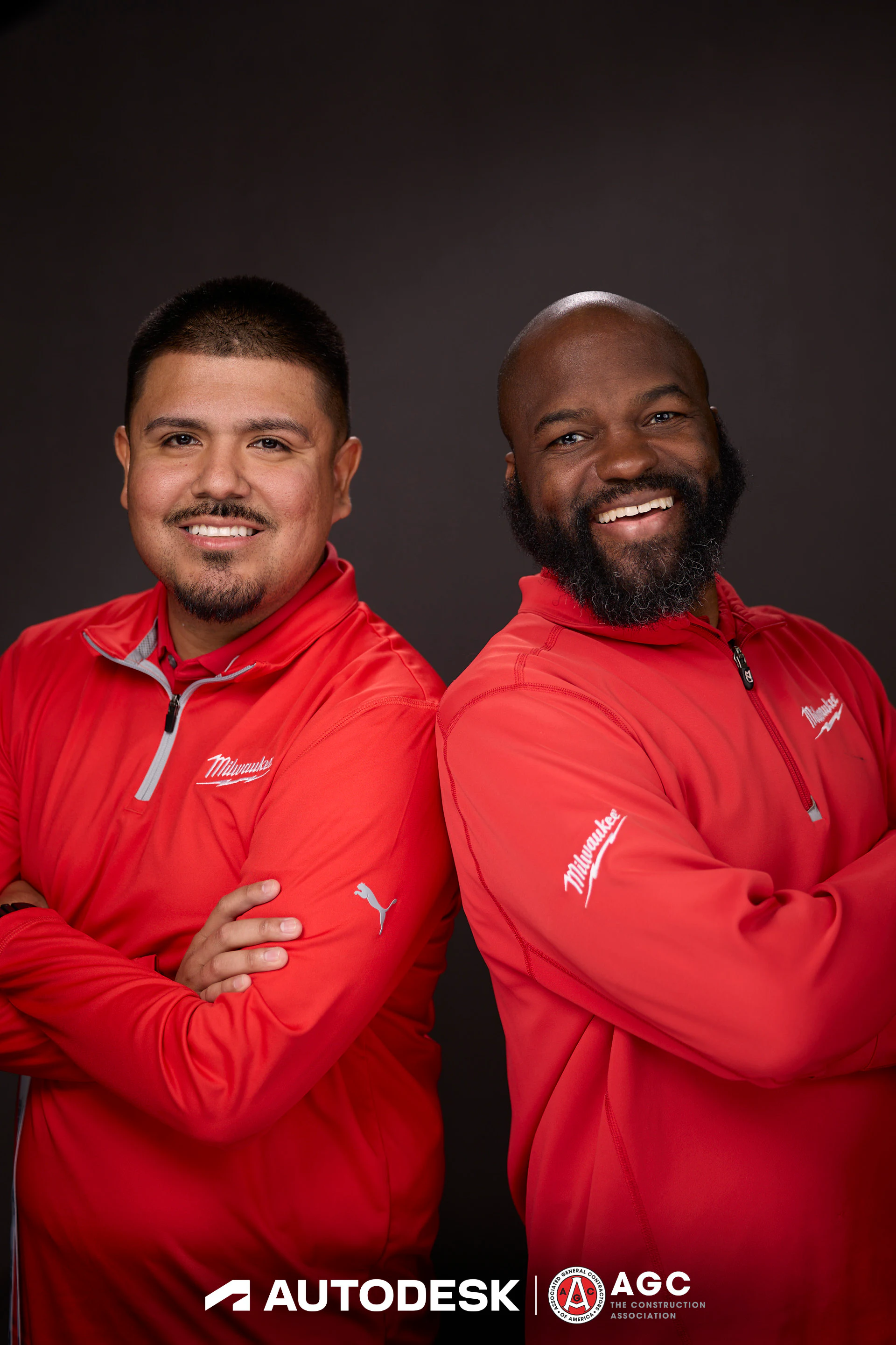 Two guests in red quarter-zips back to back with their arms folded at Autodesk at the AGC Annual Convention 2025