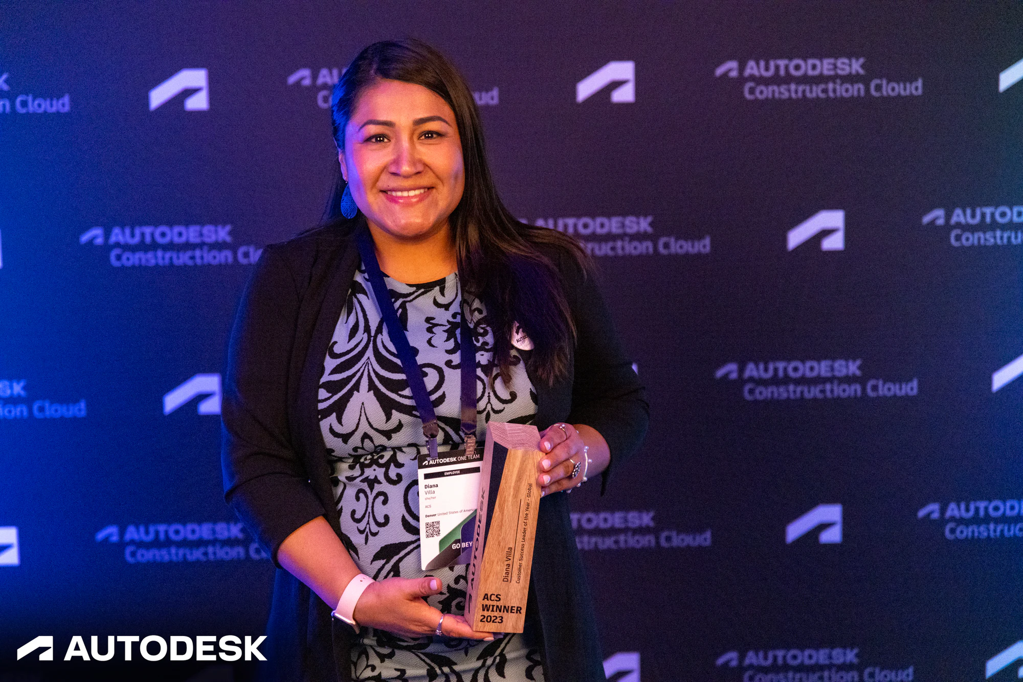An award winner holding her ACS Winner 2023 trophy at the Autodesk backdrop at the Autodesk OTC Awards 2023