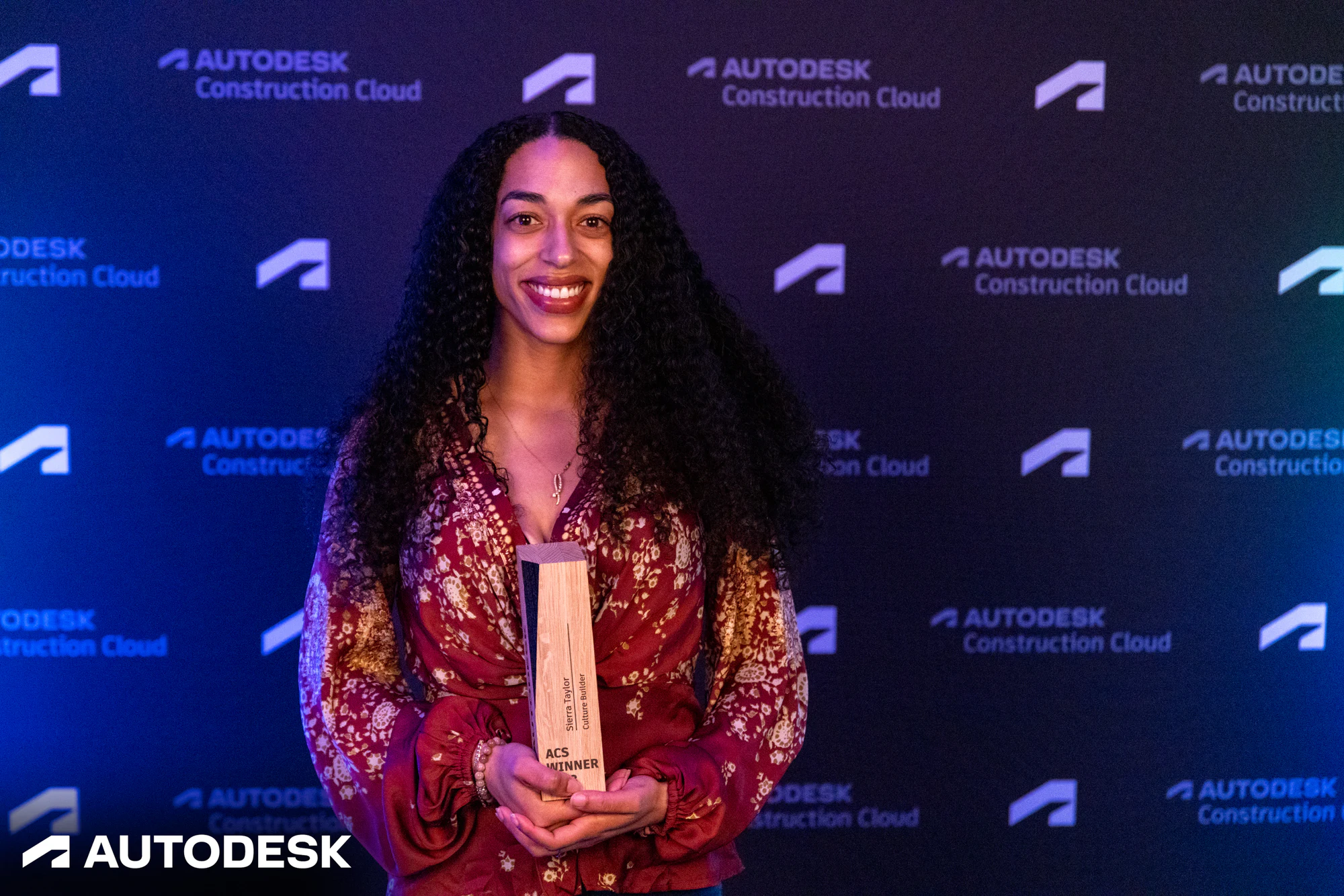 An award winner in a red floral top holding her ACS Winner trophy at the Autodesk OTC Awards 2023