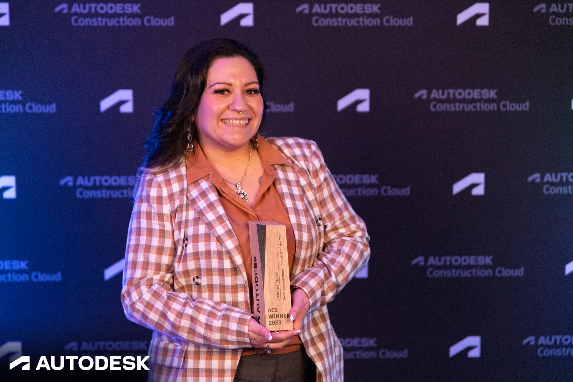 An award winner in a checked blazer holding her ACS Winner 2023 trophy at the Autodesk OTC Awards 2023