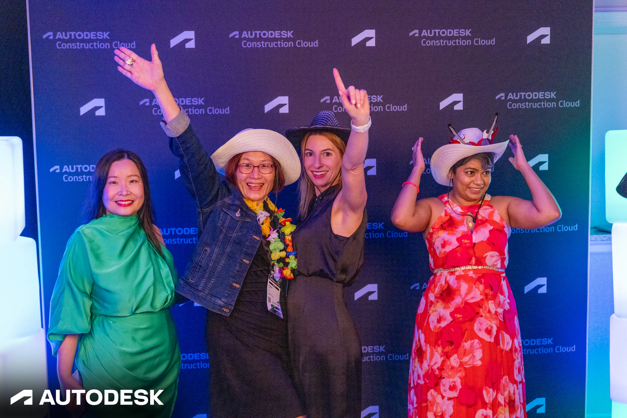 Four guests in cowboy hats and leis cheering at the Autodesk Construction Cloud backdrop at the Autodesk OTC Awards 2023
