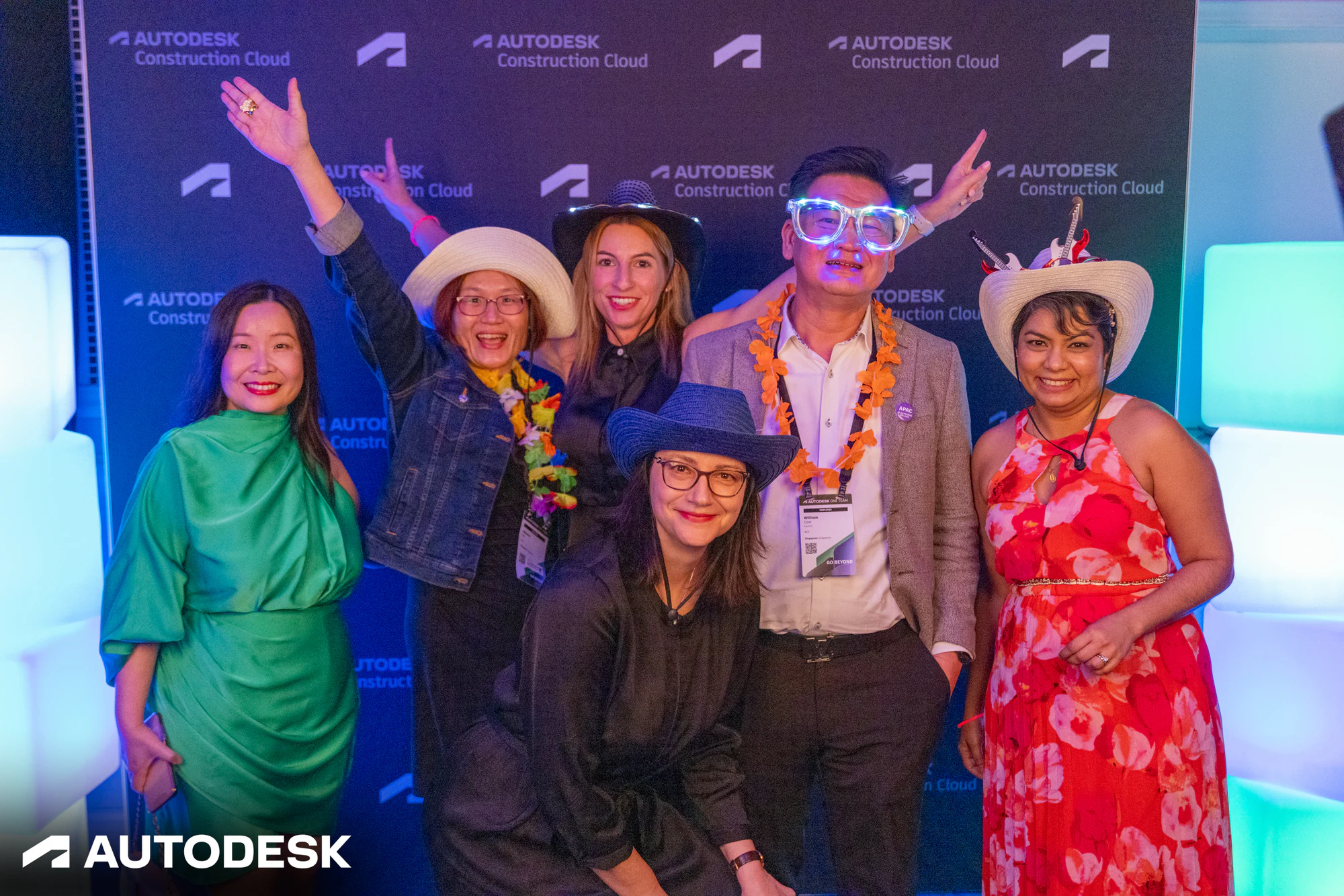 Six guests in hats, leis and light-up glasses posing together at the backdrop at the Autodesk OTC Awards 2023