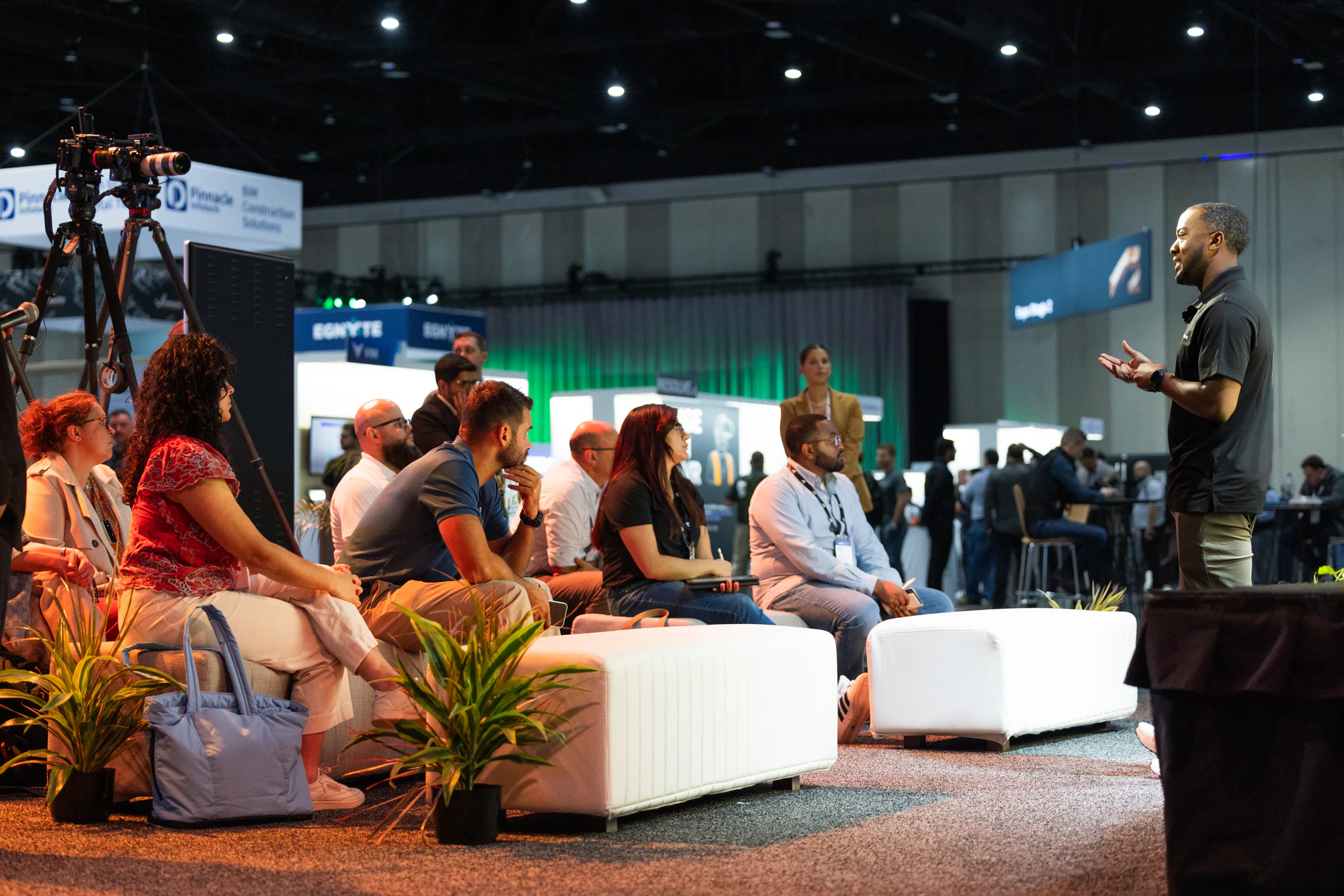 The same lounge session from the side, the audience on white benches and a camera on a tripod behind them at Autodesk University 2024