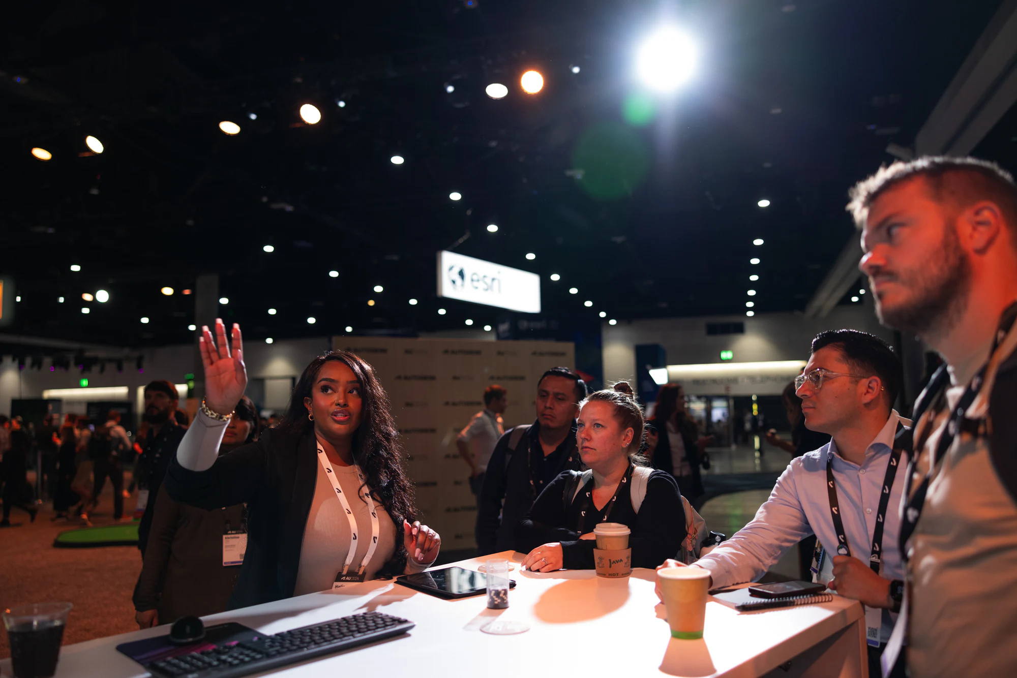The specialist raising a hand mid-explanation while the group around the demo table leans in at Autodesk University 2024