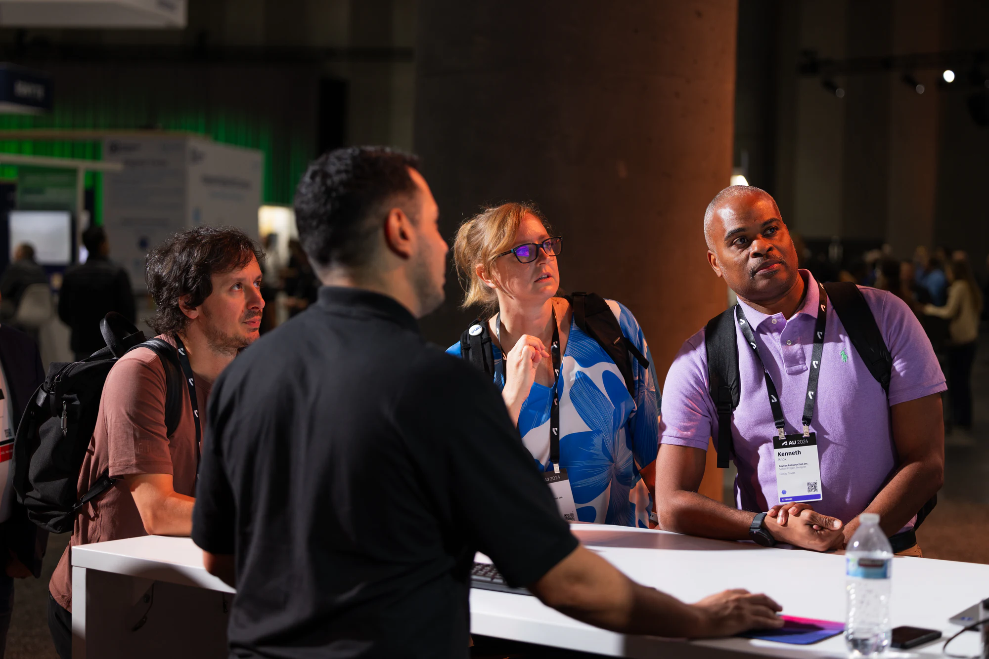 The same three attendees watching closely as the staffer points to the screen at Autodesk University 2024
