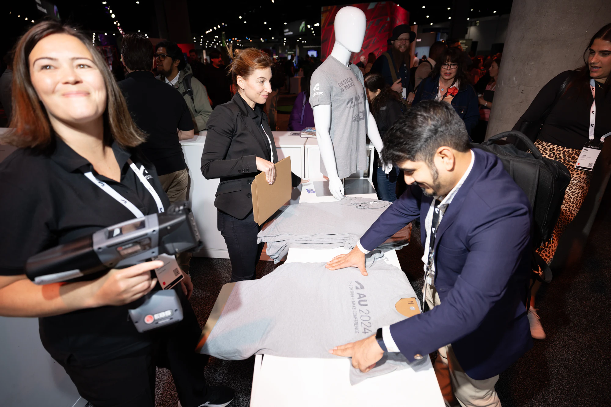 A staffer laughing as she holds the press while an attendee smooths out his T-shirt at Autodesk University 2024