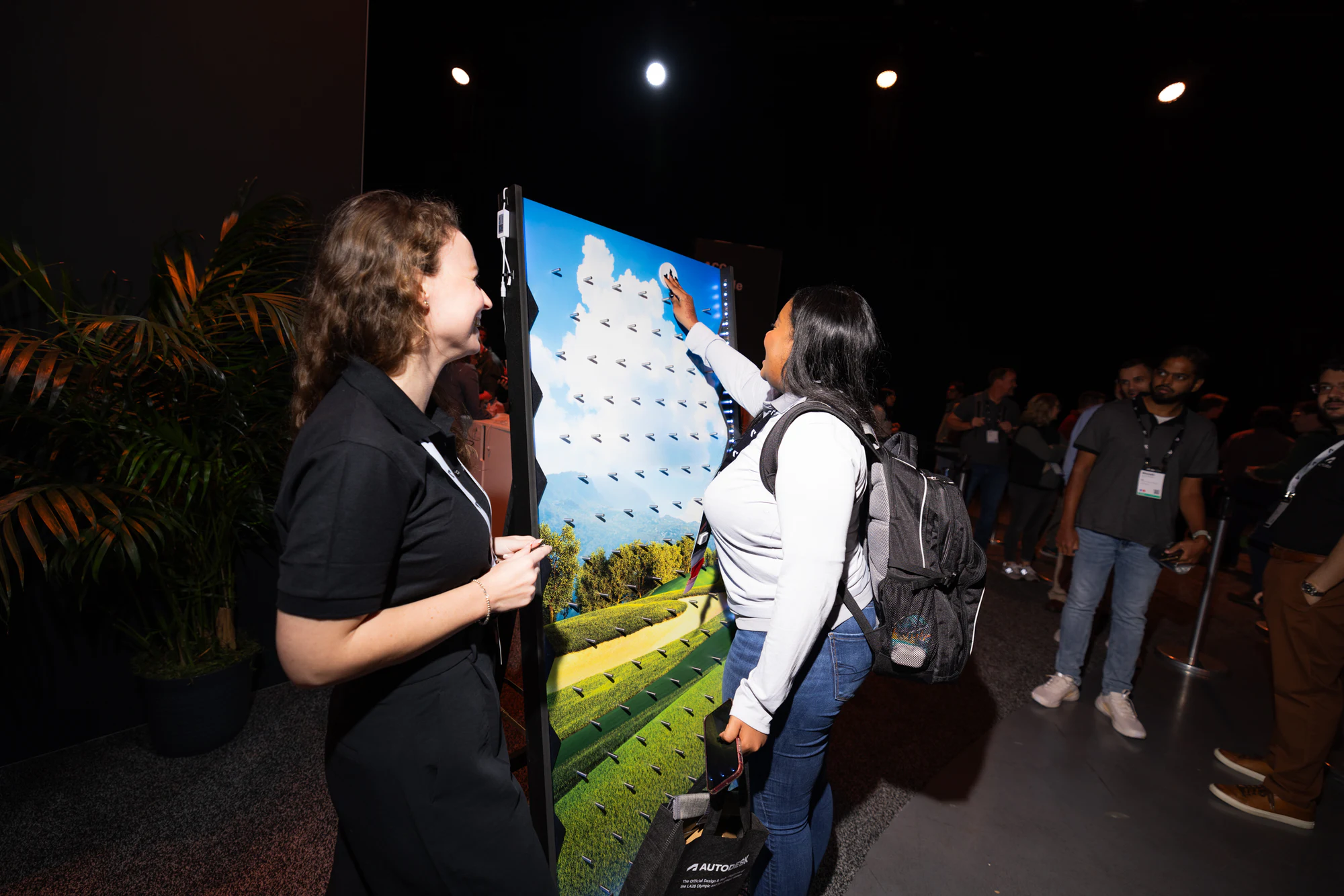 The attendee pressing pins into the wall's landscape picture while the staffer looks on at Autodesk University 2024