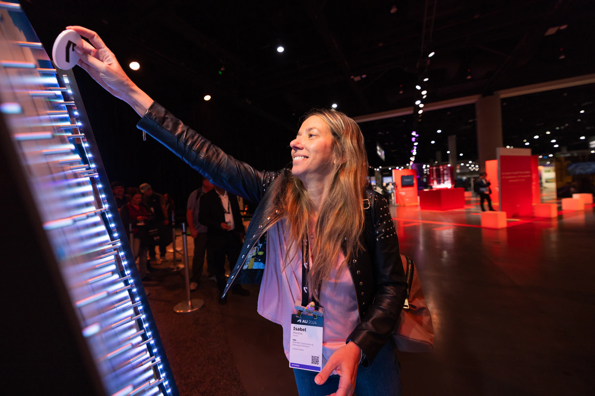 An attendee smiling as she reaches up to push a pin on a lit pin wall at Autodesk University 2024