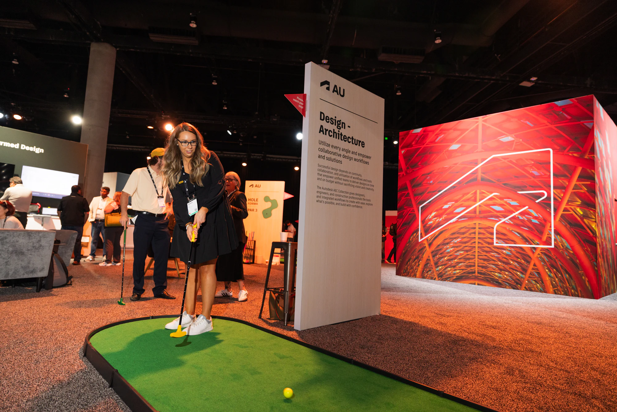 An attendee lining up a putt on the show-floor mini-golf hole by the Design and Architecture sign at Autodesk University 2024