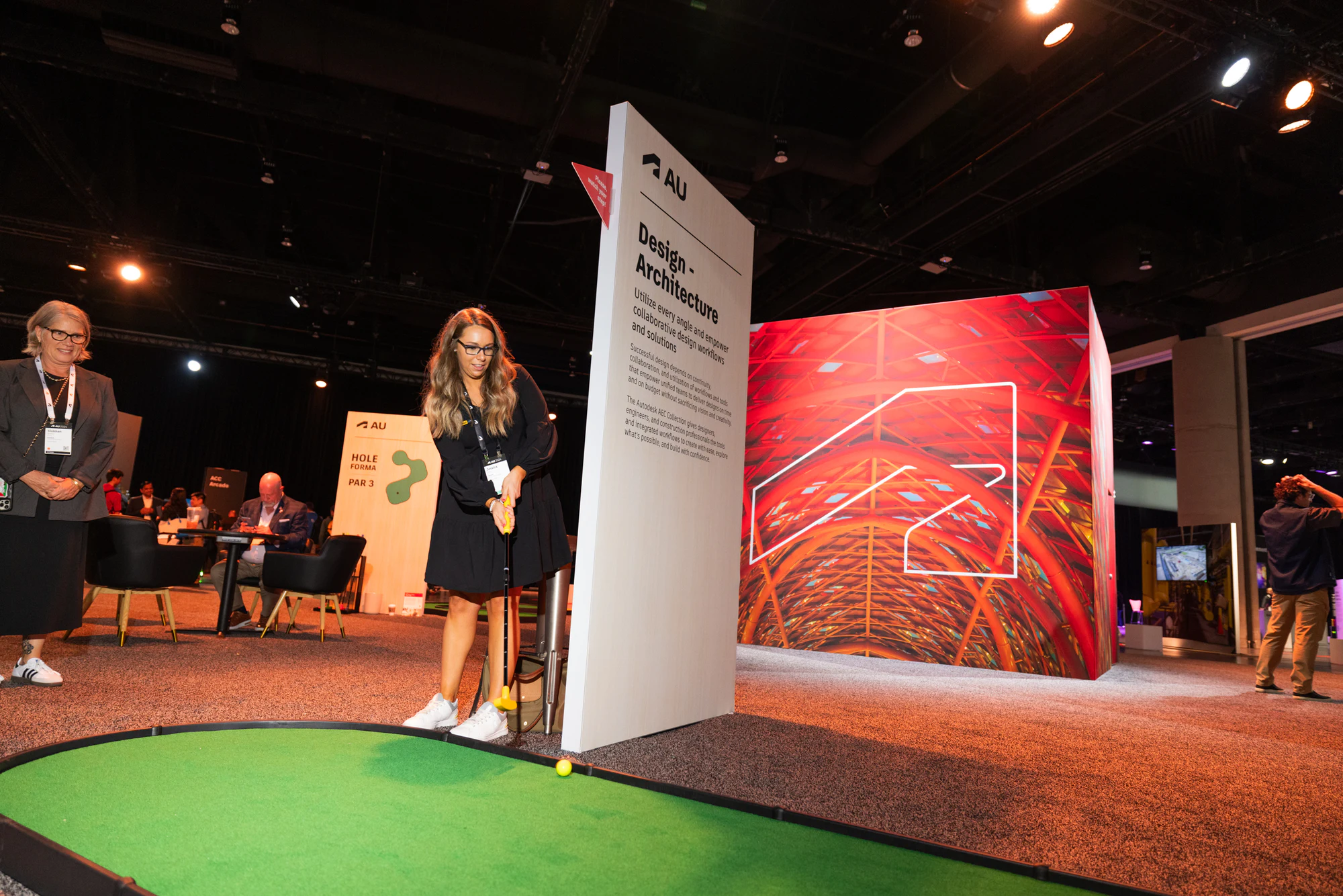 Her putt rolling toward the cup as another attendee watches from beside the green at Autodesk University 2024
