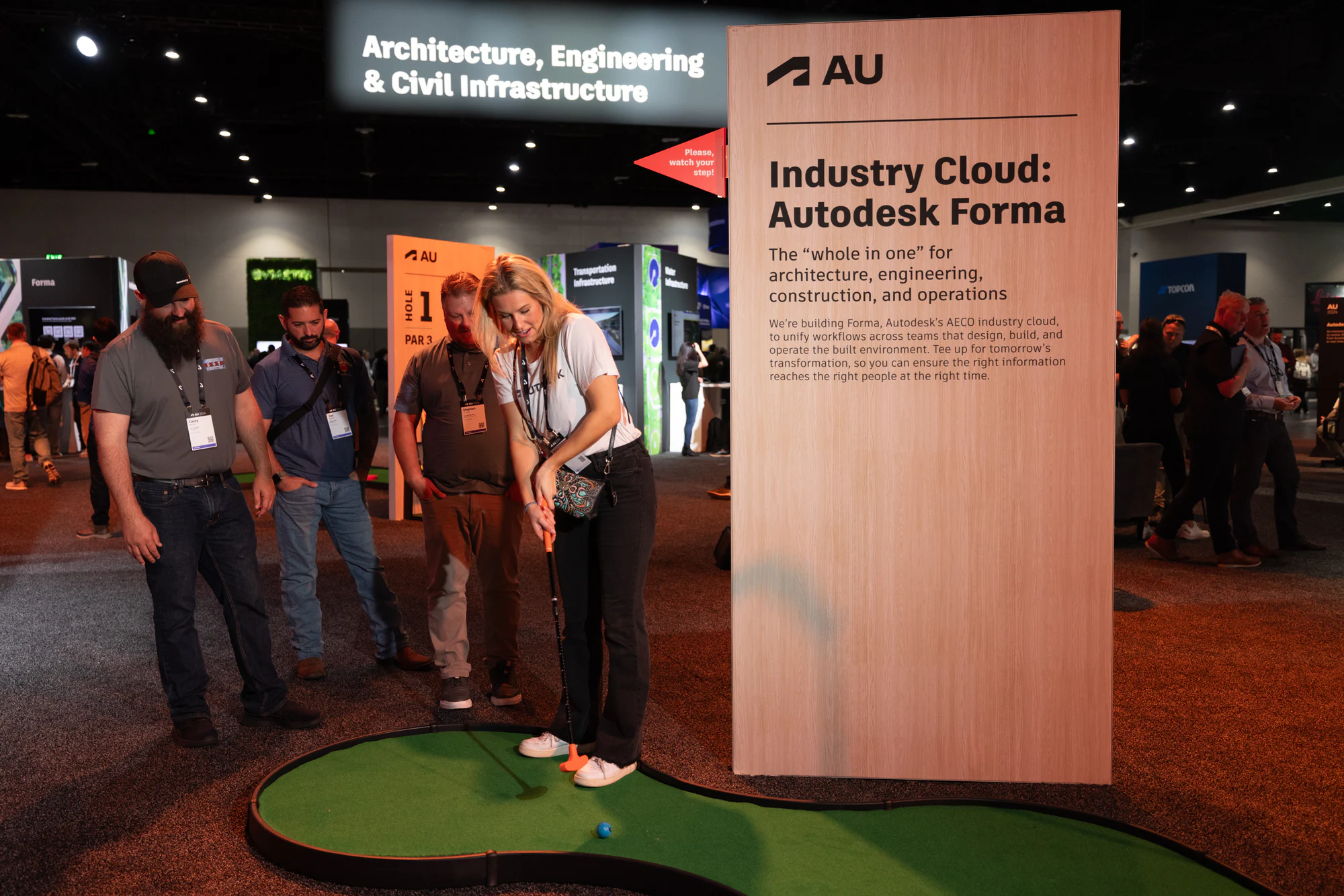 An attendee putting on the mini-golf hole by the Autodesk Forma sign, her group watching at Autodesk University 2024