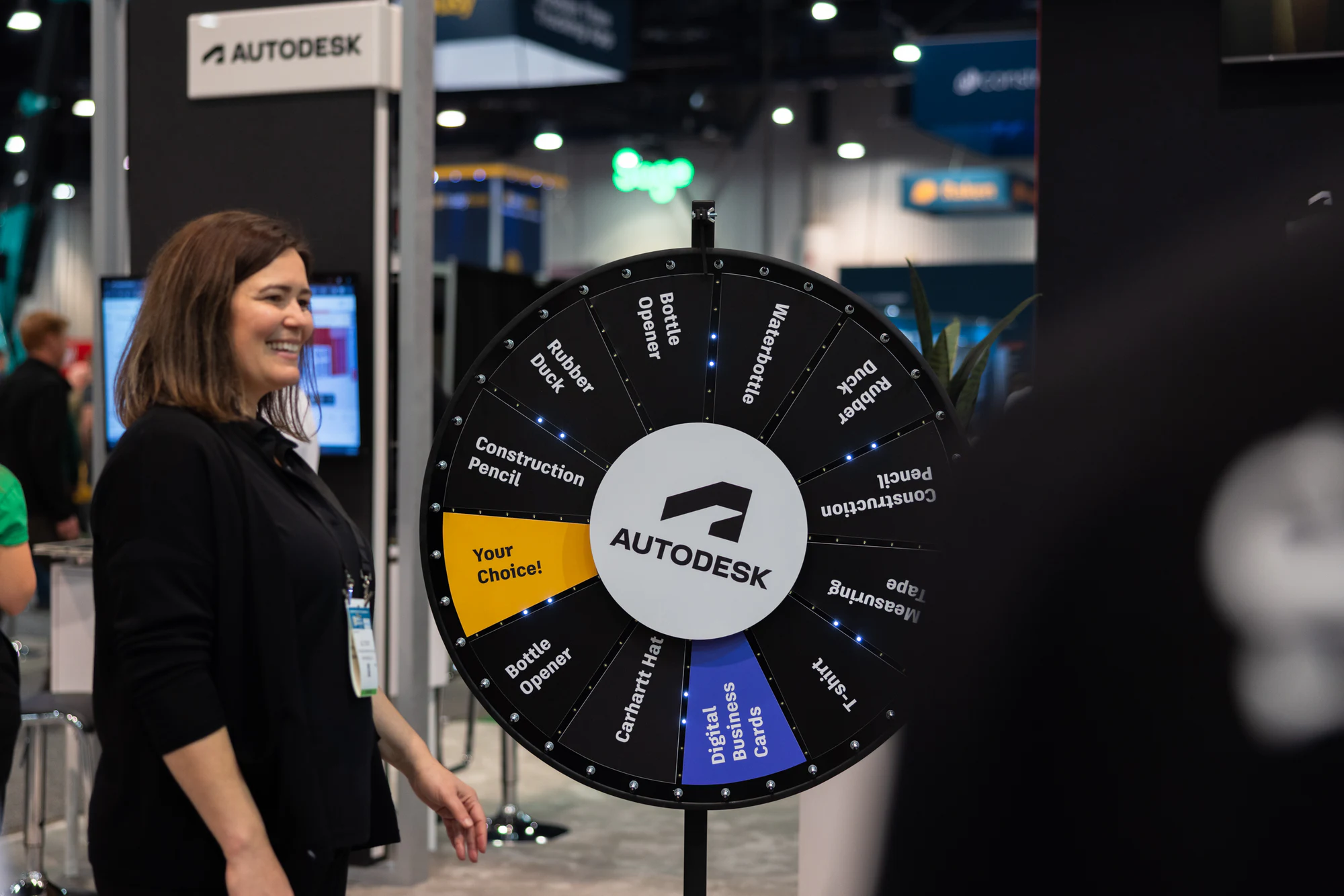 An Autodesk team member smiling beside the prize wheel on the booth at Autodesk at World of Concrete 2024