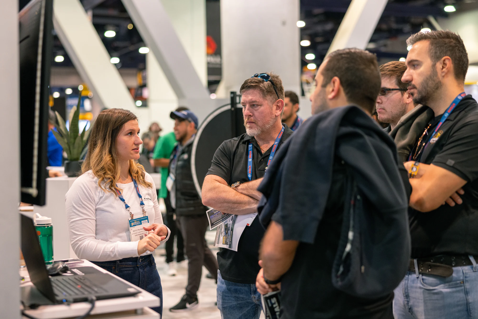 An Autodesk team member talking with visitors in black shirts at a demo station at Autodesk at World of Concrete 2024