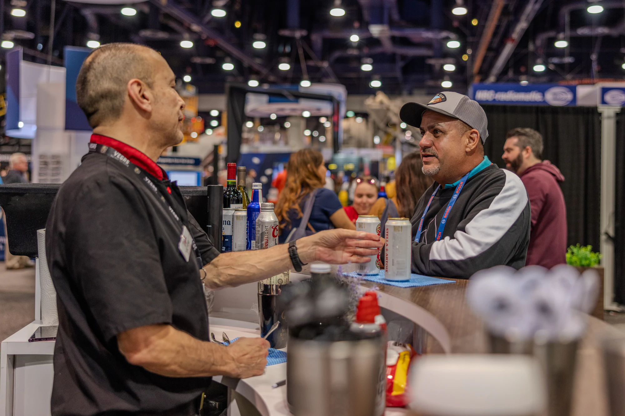 Two visitors talking across the booth’s bar counter, one holding a can at Autodesk at World of Concrete 2024