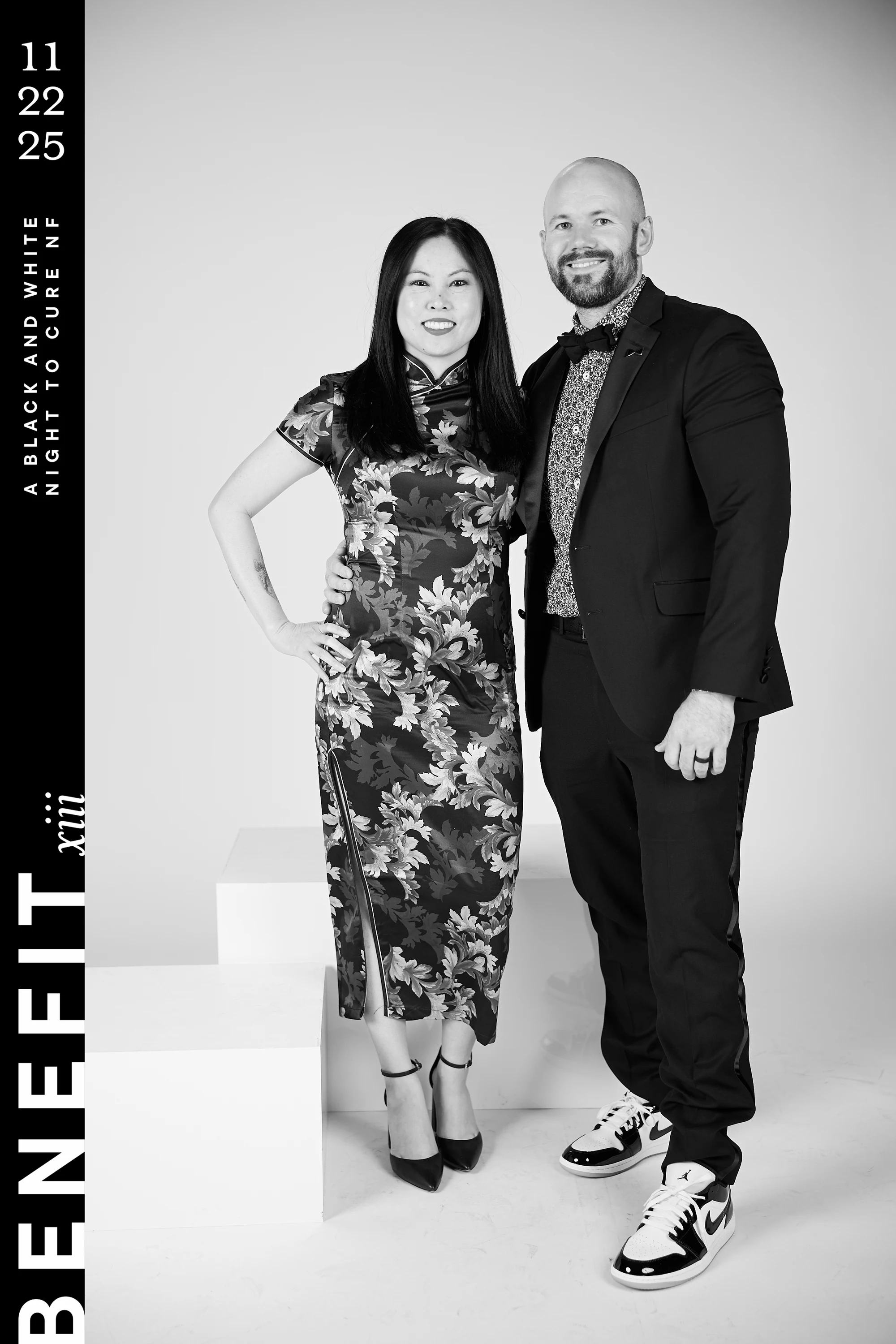 Black and white portrait of a couple arm in arm, her in a floral high-collar dress, him in a suit and sneakers at beNeFit XIII