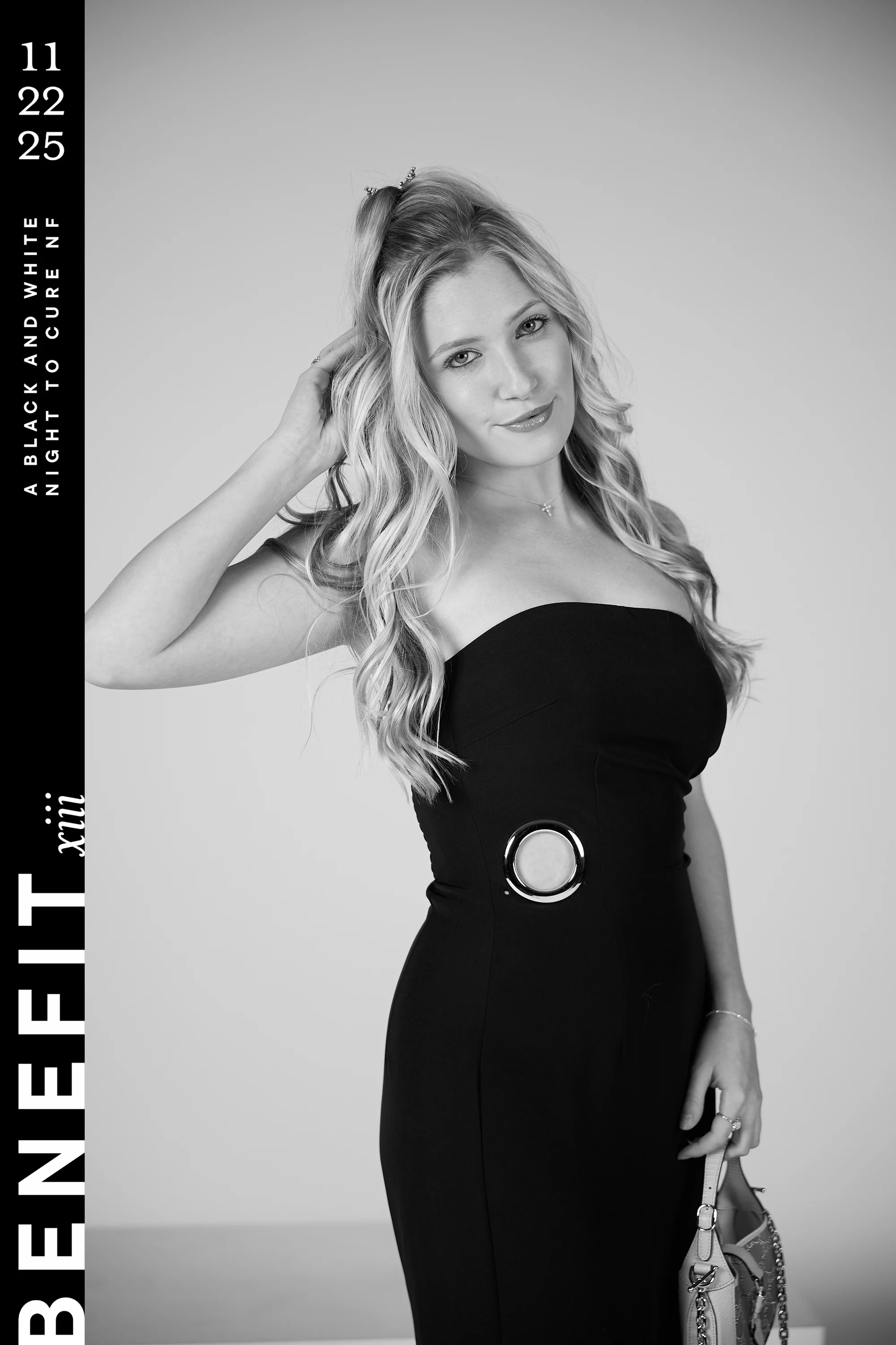 Black and white portrait of a woman in a strapless black dress, one hand in her hair at beNeFit XIII