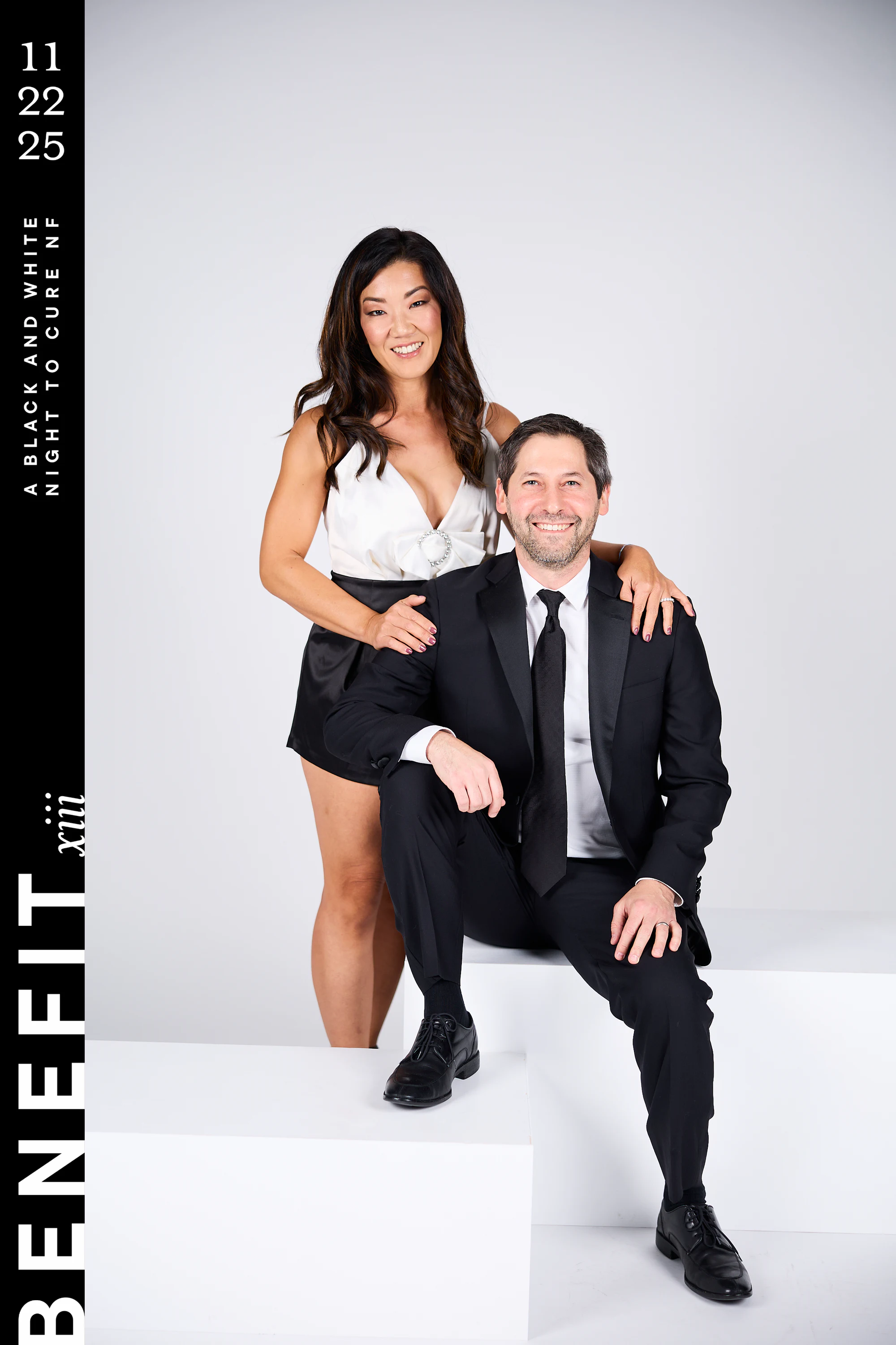 The same couple full length, him seated on the block with a foot forward at beNeFit XIII