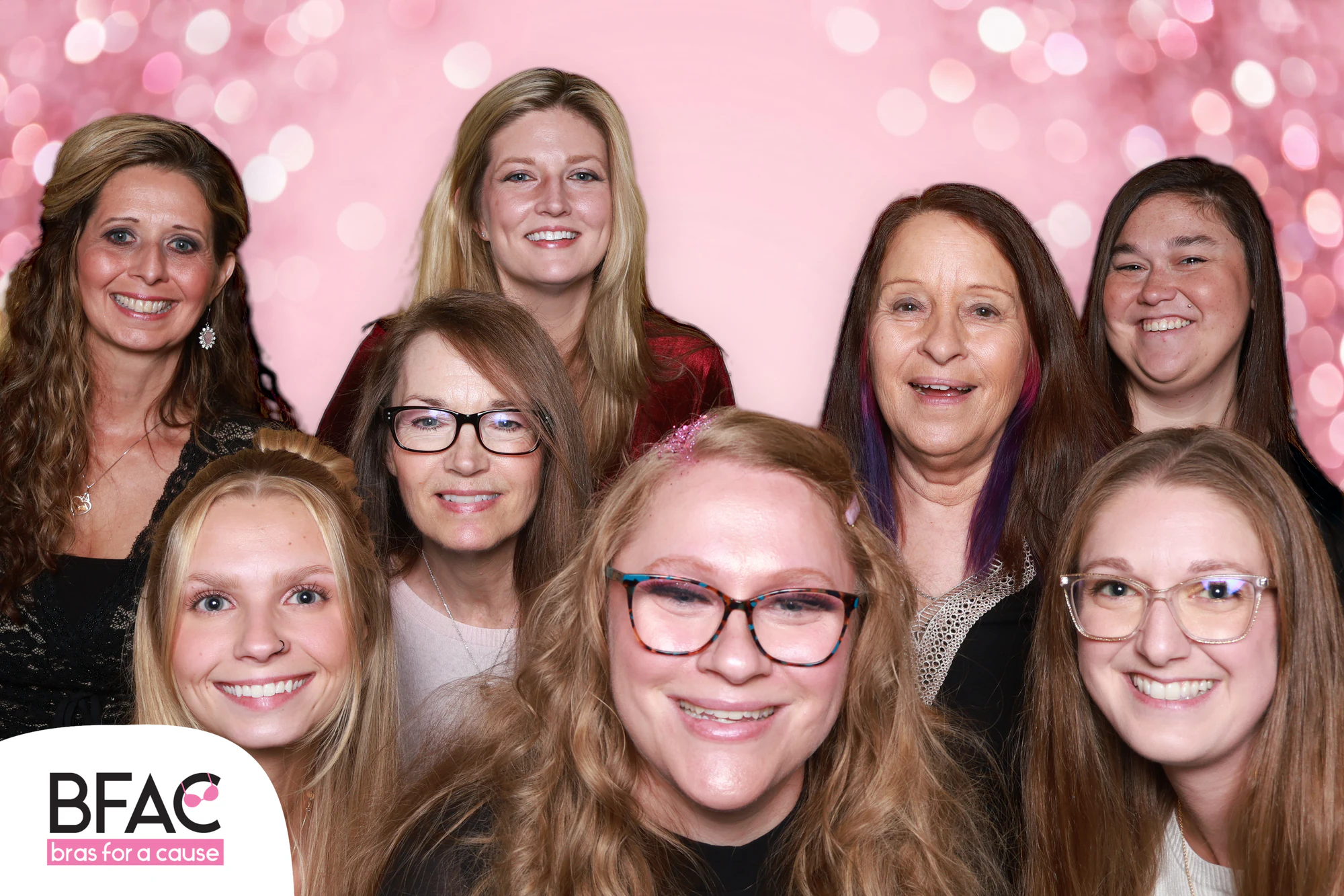 Eleven women packed close together on a pink sparkle background at Bras for a Cause 2026