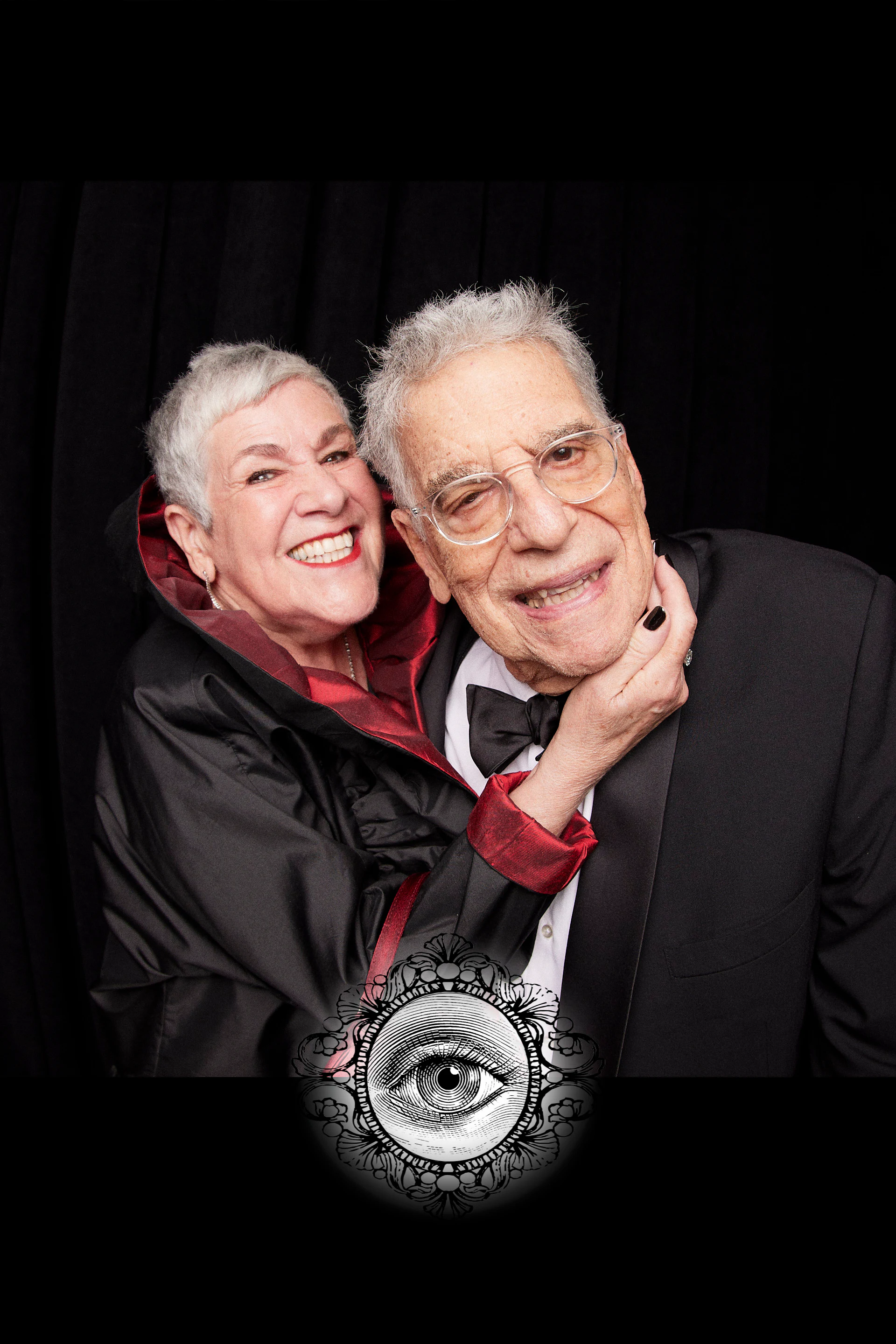 A guest in a black cape hugging a guest in a tuxedo from behind at the carnivalesque wedding at the Fisher Building