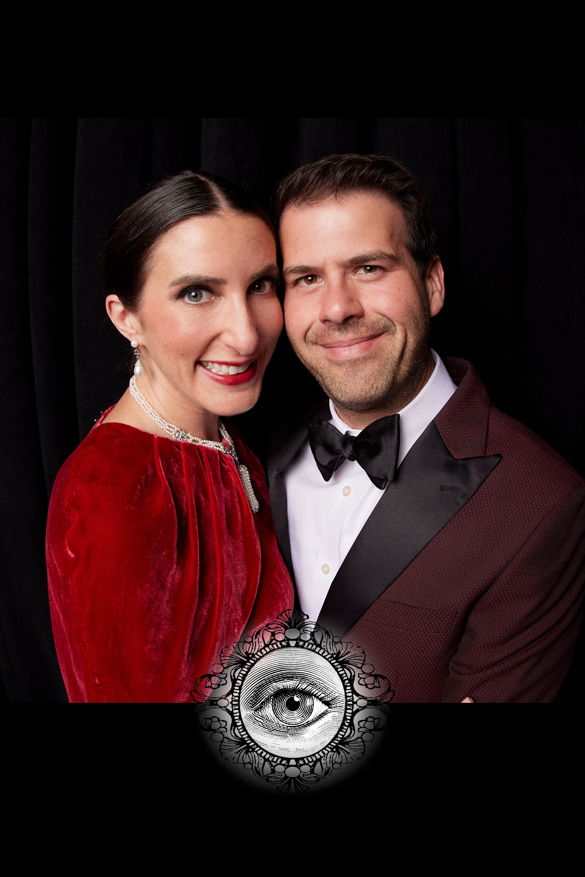 A guest in a red velvet dress and a guest in a burgundy tuxedo, cheek to cheek at the carnivalesque wedding at the Fisher Building
