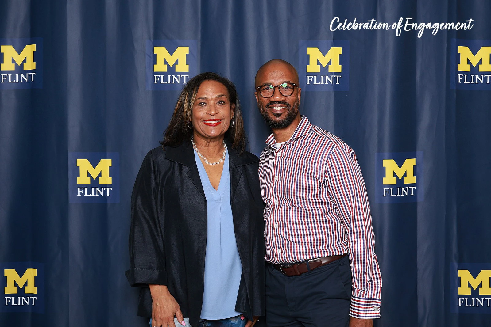 A woman in a navy jacket and a man in a striped shirt, shoulder to shoulder, both smiling at Celebration of Engagement