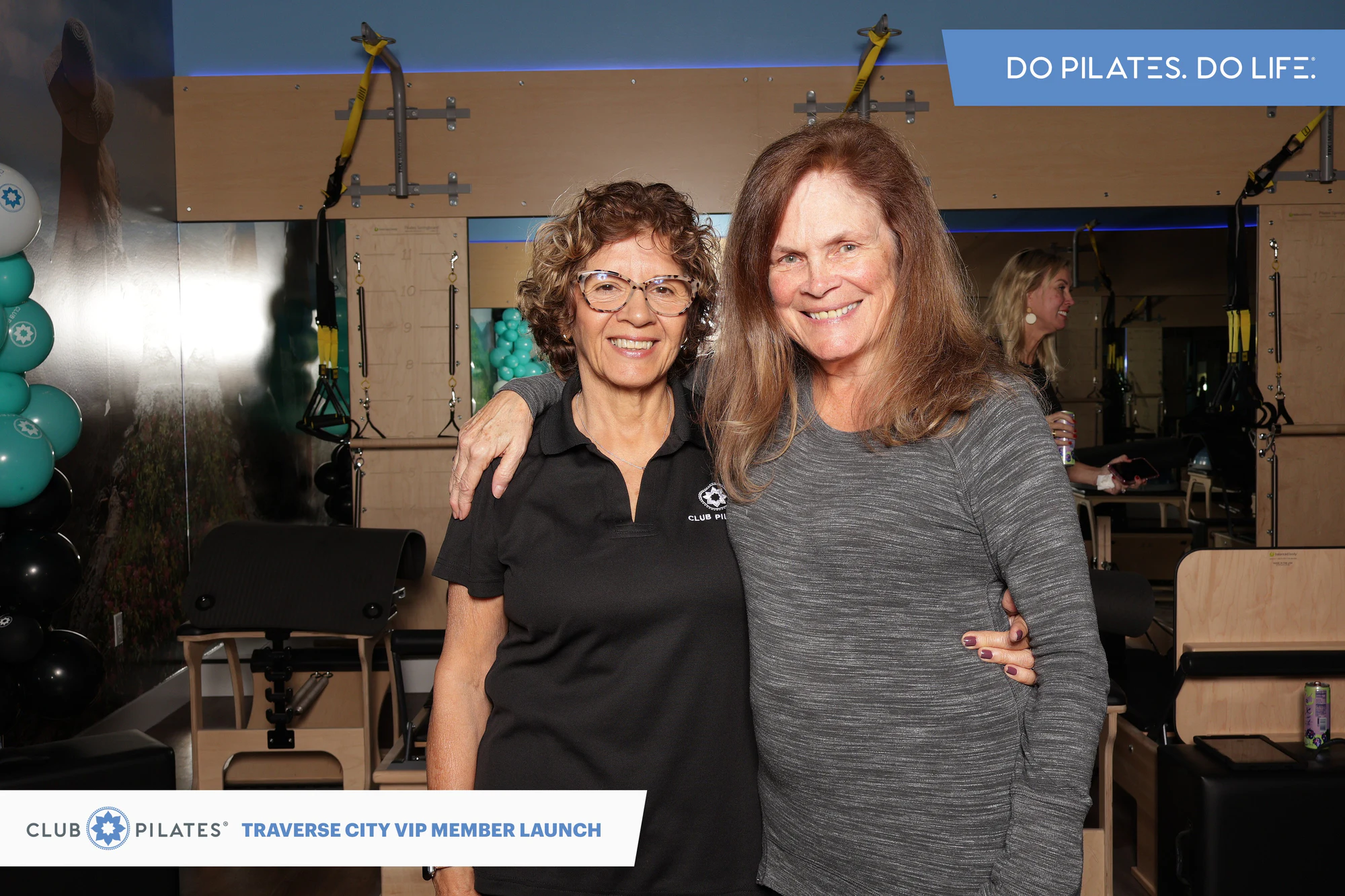 Two women with their arms around each other, one in a black Club Pilates polo and one in a gray top at Club Pilates Traverse City