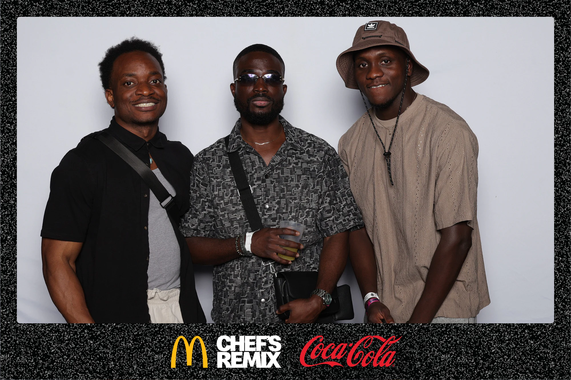 Three guests at the backdrop, one in a bucket hat, one holding a drink at Coca-Cola x McDonald’s at the Jerk x Jollof Afterparty
