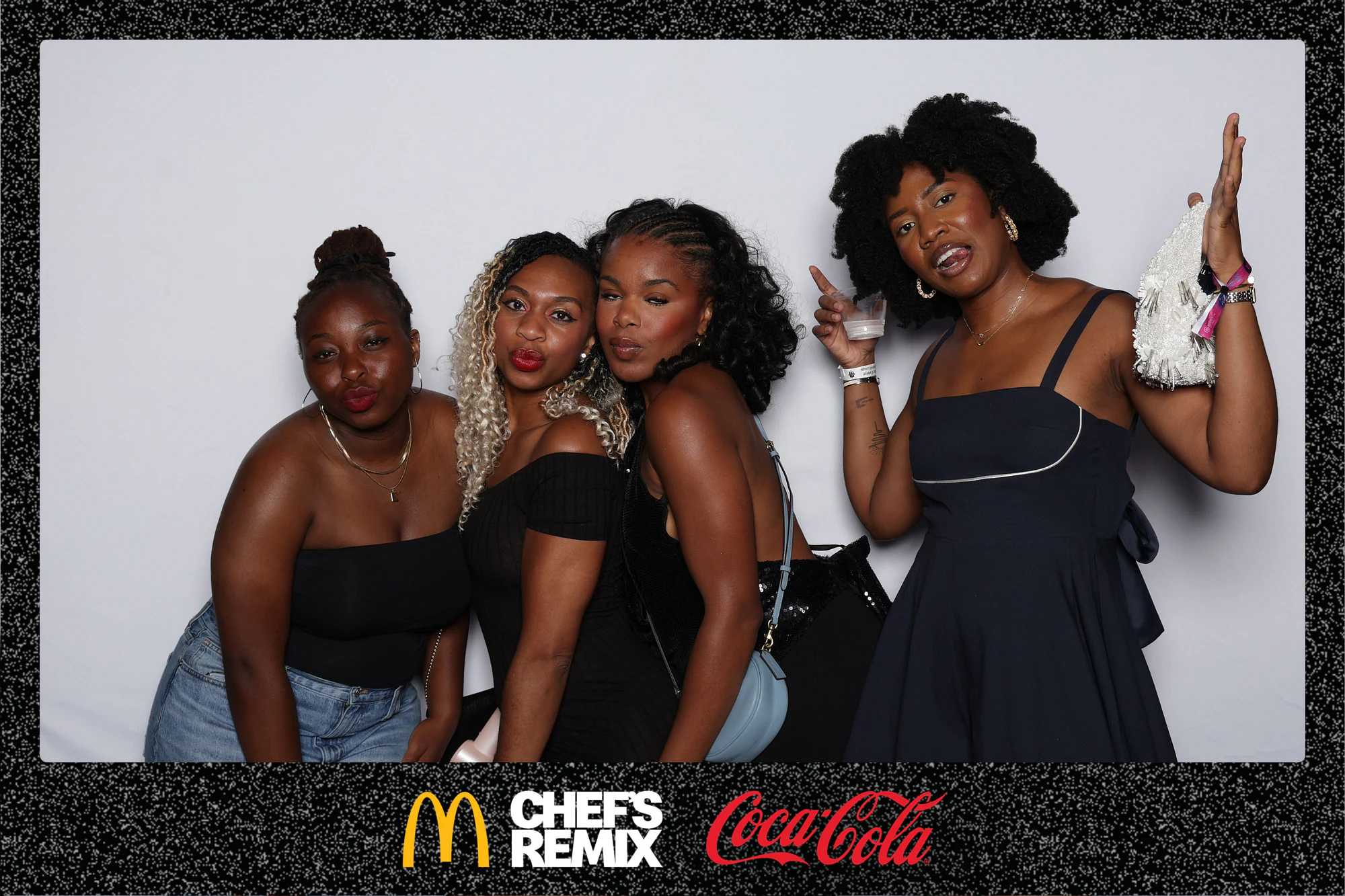 Four guests leaning in, one with a drink and a white pom-pom raised at Coca-Cola x McDonald’s at the Jerk x Jollof Afterparty