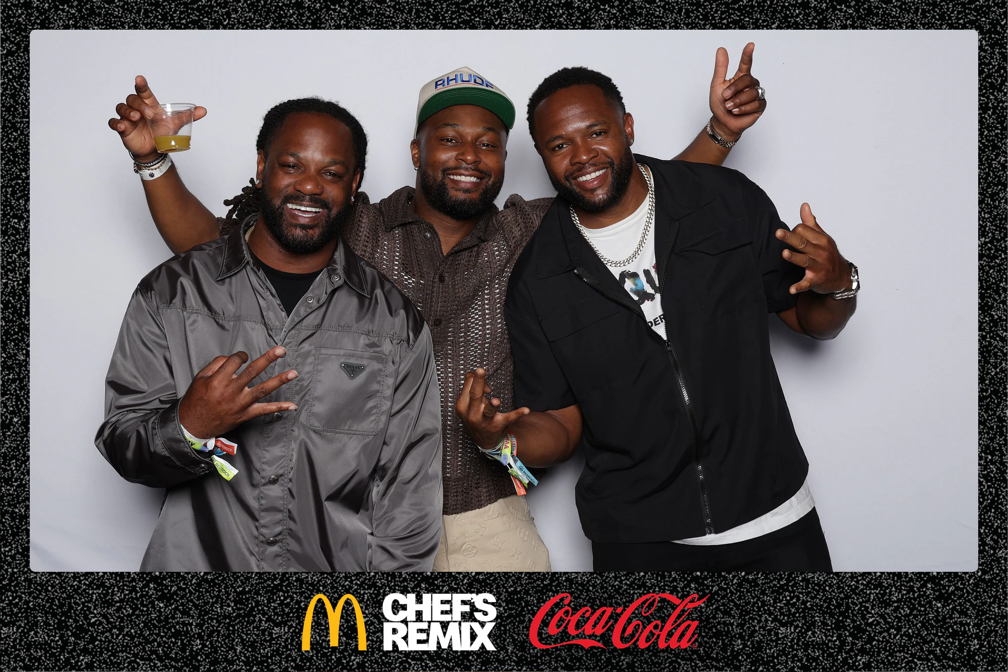 Three guests with their hands up, one holding a drink, against the white backdrop at Coca-Cola x McDonald’s at the Jerk x Jollof Afterparty