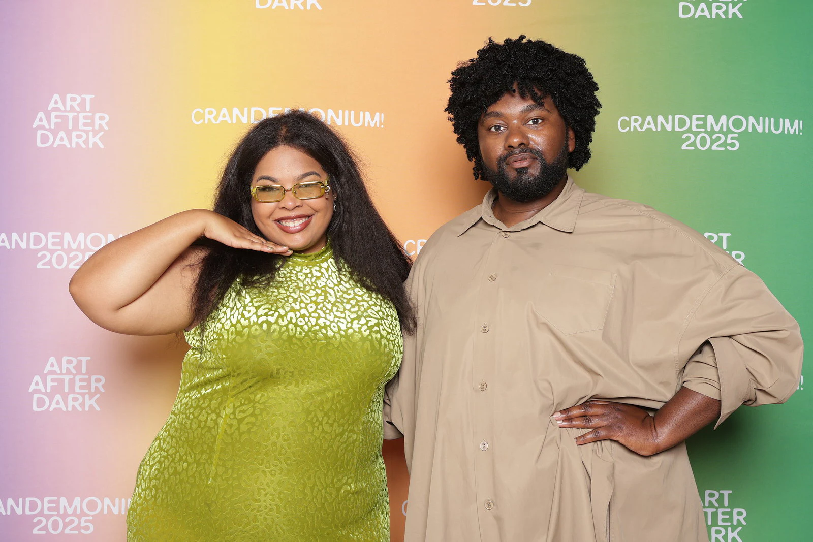 A woman in a lime sequin dress with a hand under her chin and a man in a tan shirt with hands on his hips in front of a pastel gradient background printed with the event’s name